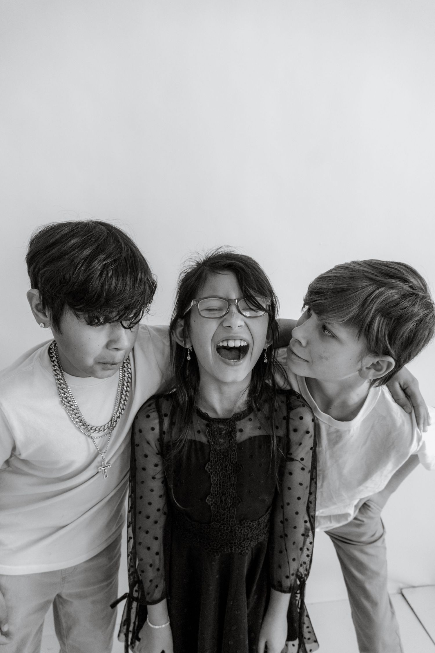 Black and white portrait of three young people laughing and posing together against a white background.