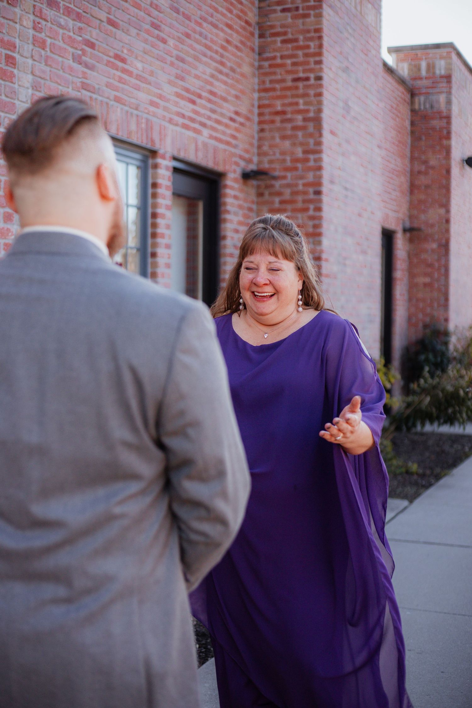 Wedding couple sharing a candid moment against a red brick building exterior.