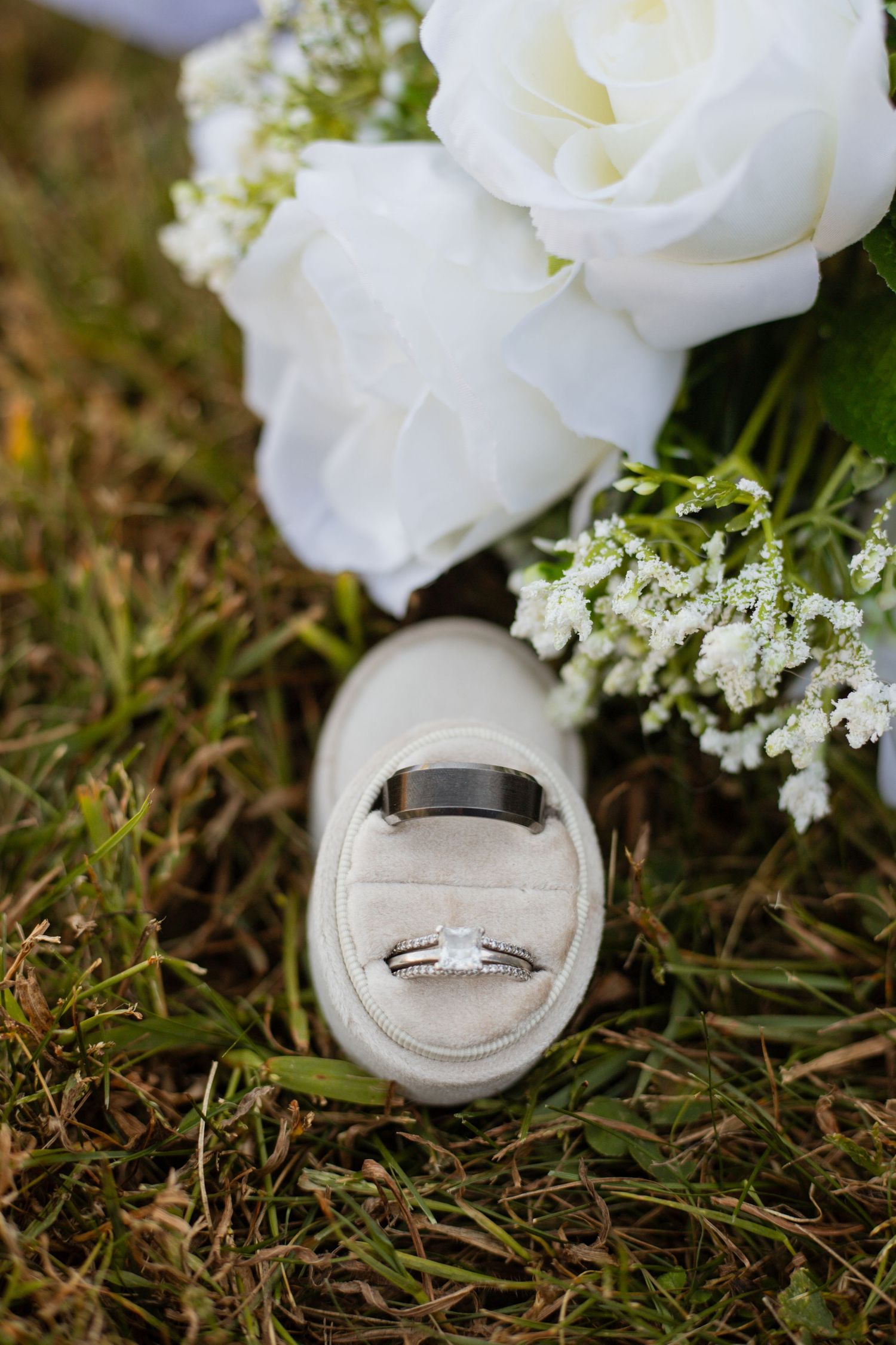 Wedding rings nestled among white roses and baby's breath flowers on grass.