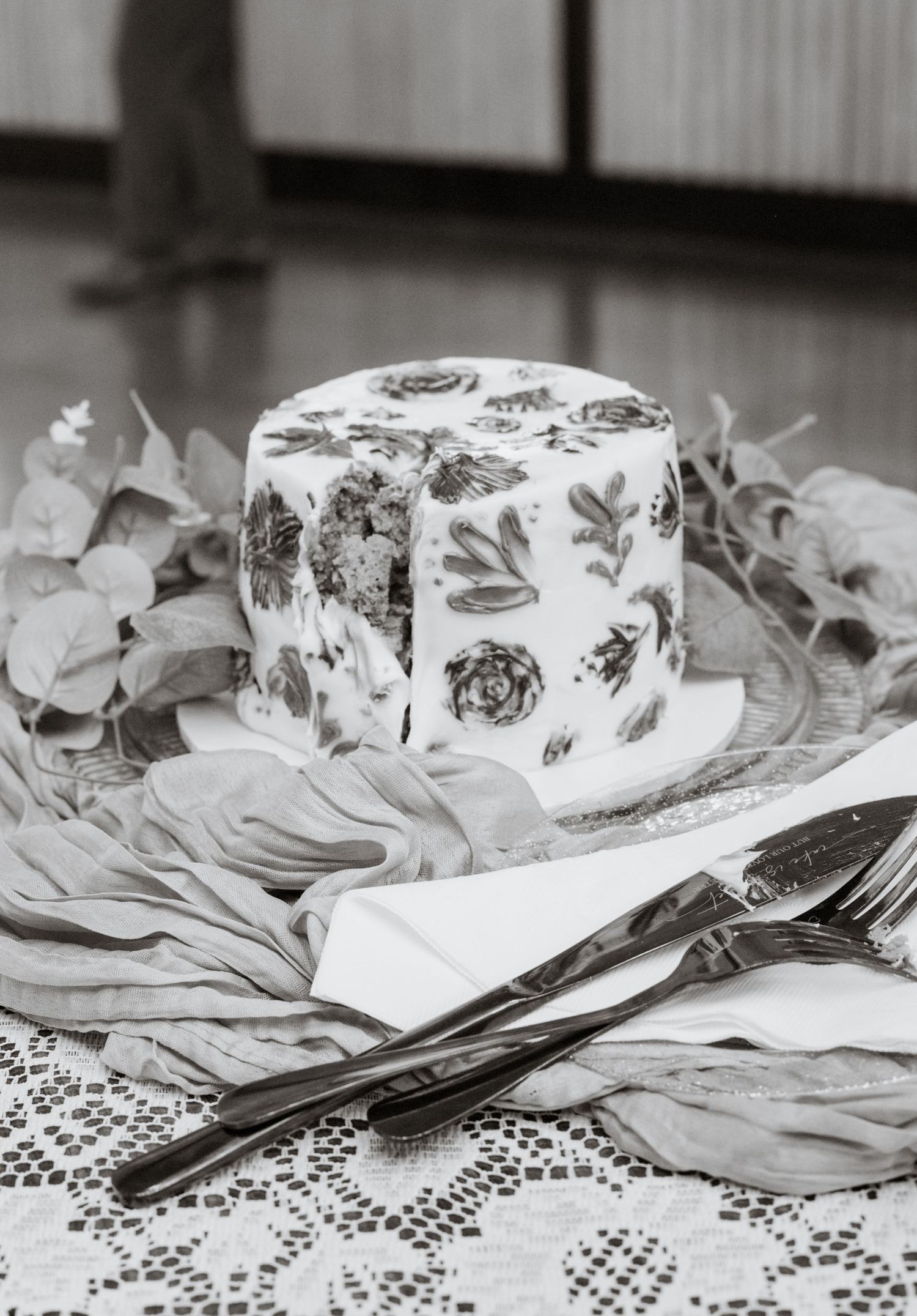 A small white wedding cake decorated with floral designs sits on a lace tablecloth.