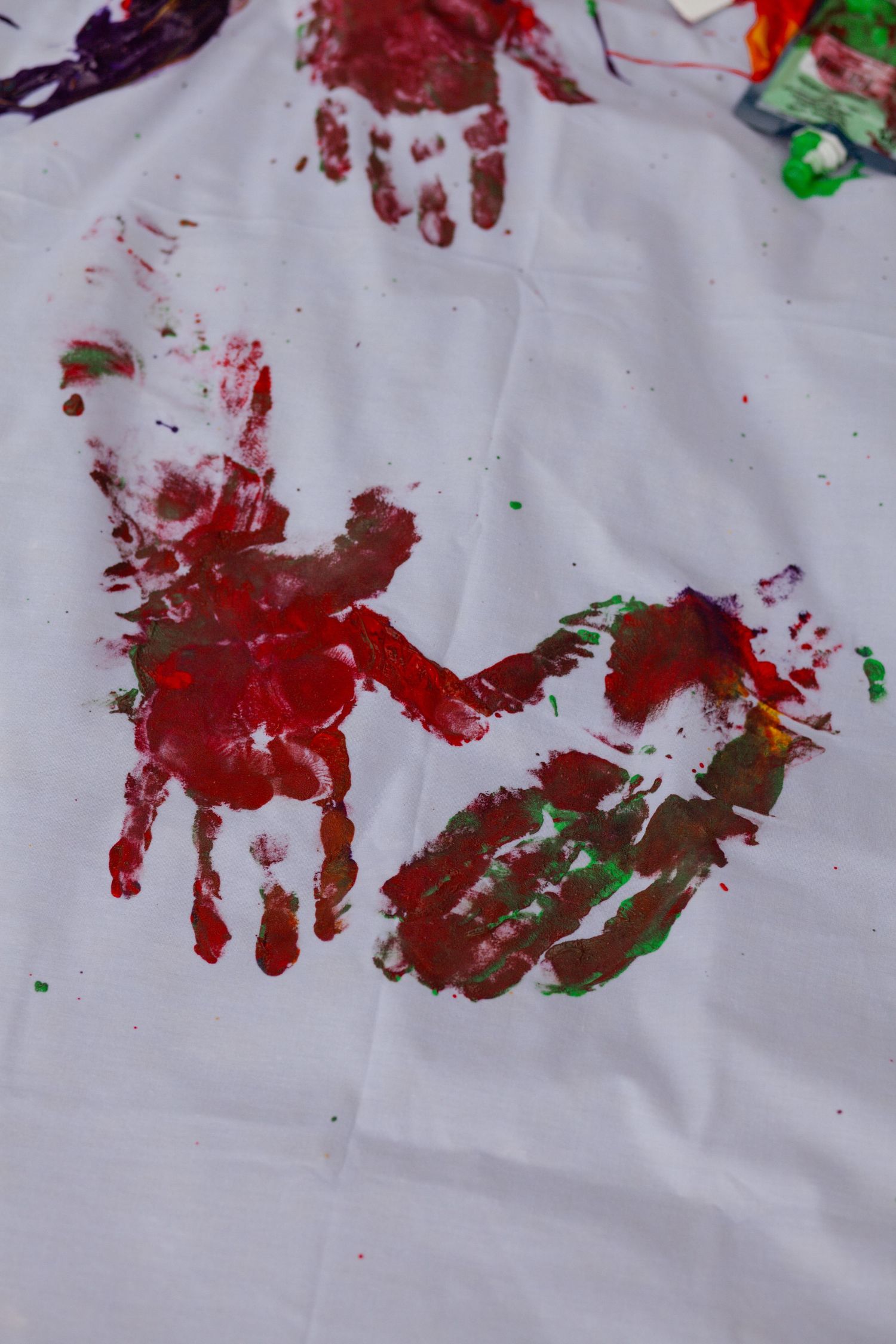 Red and green handprints scattered across white fabric create abstract art patterns.