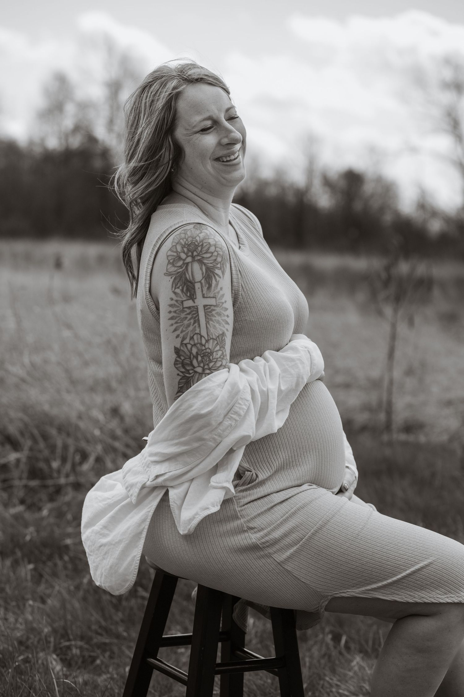 Maternity portraits showing a pregnant woman in a ribbed dress posing on a chair outdoors.