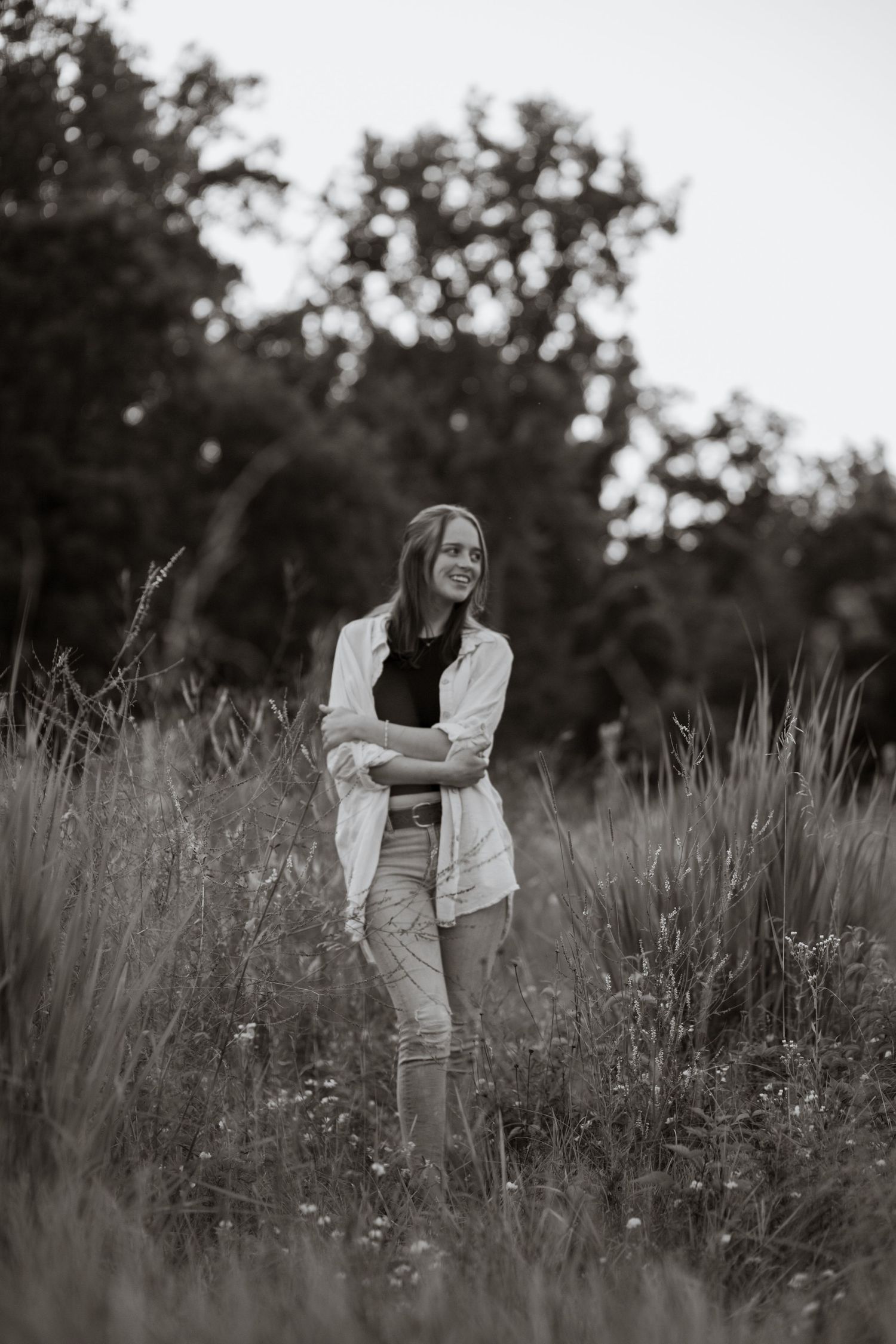 Black and white portrait of someone standing in tall grass and wildflowers.