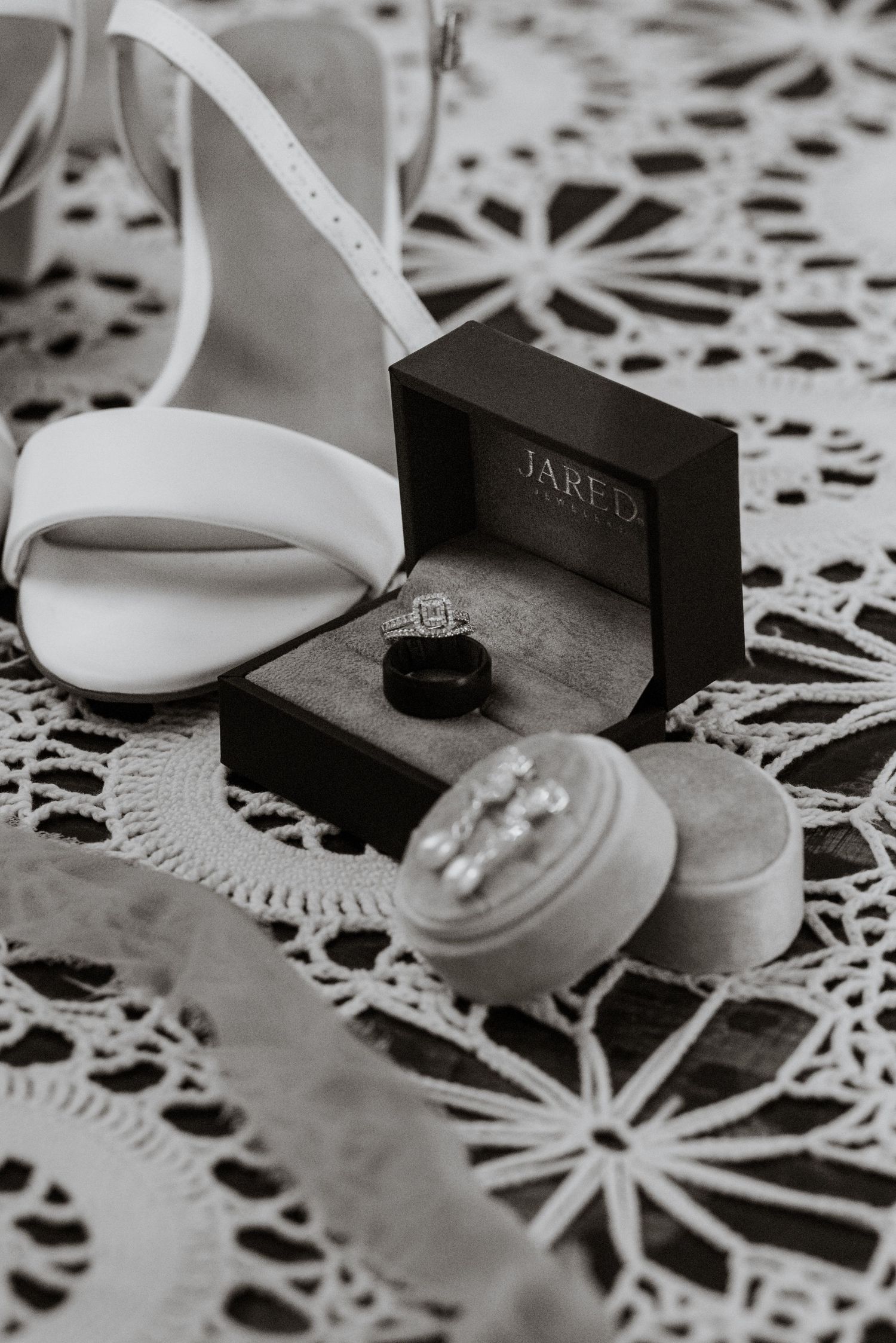 Wedding details with white sandals, rings, and lace on decorative background.