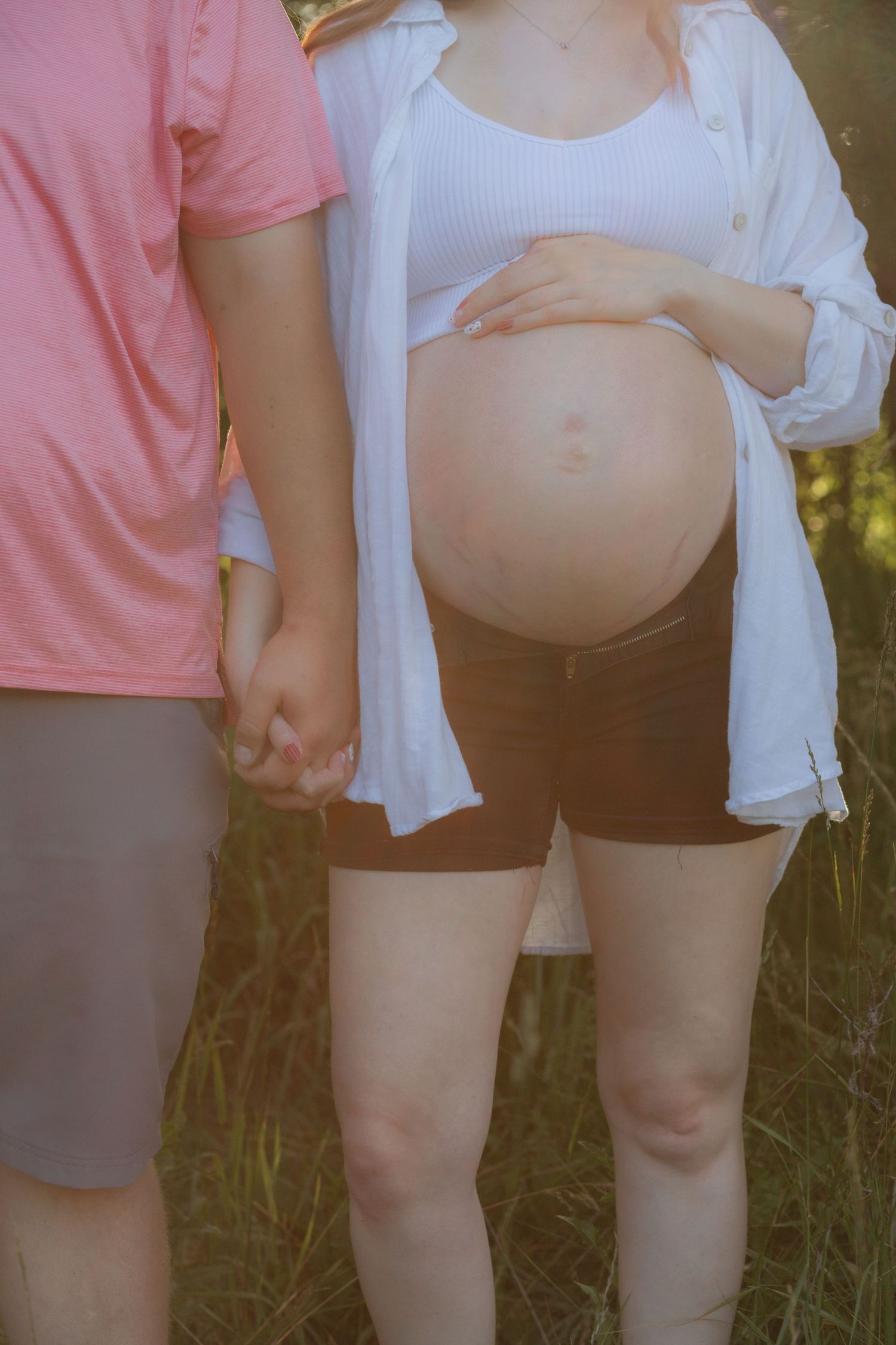 A series of photos showing a pregnant belly in a white crop top and black shorts against a sunny outdoor backdrop.