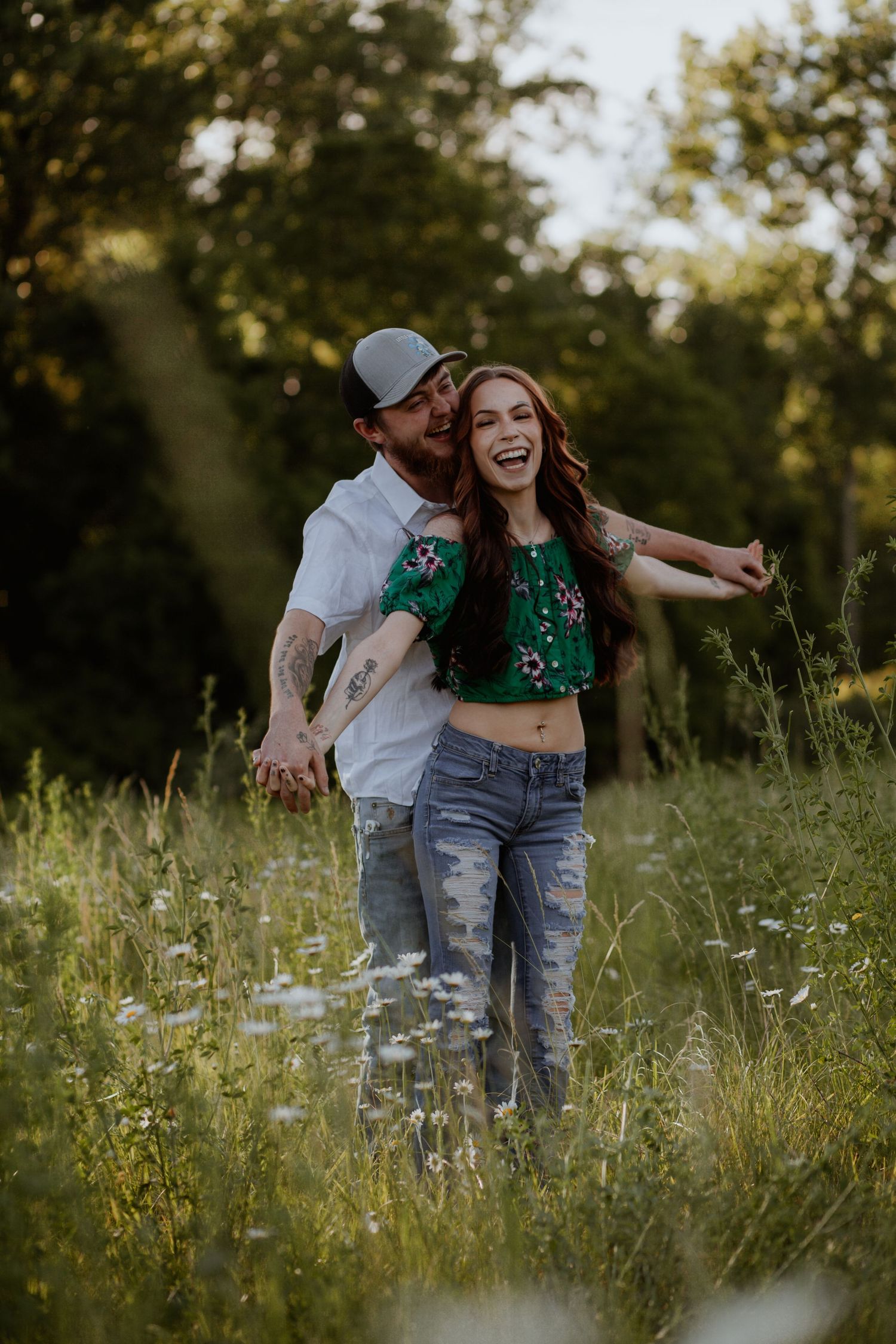 Joyful couple laughing and dancing in a field of wildflowers during sunset.