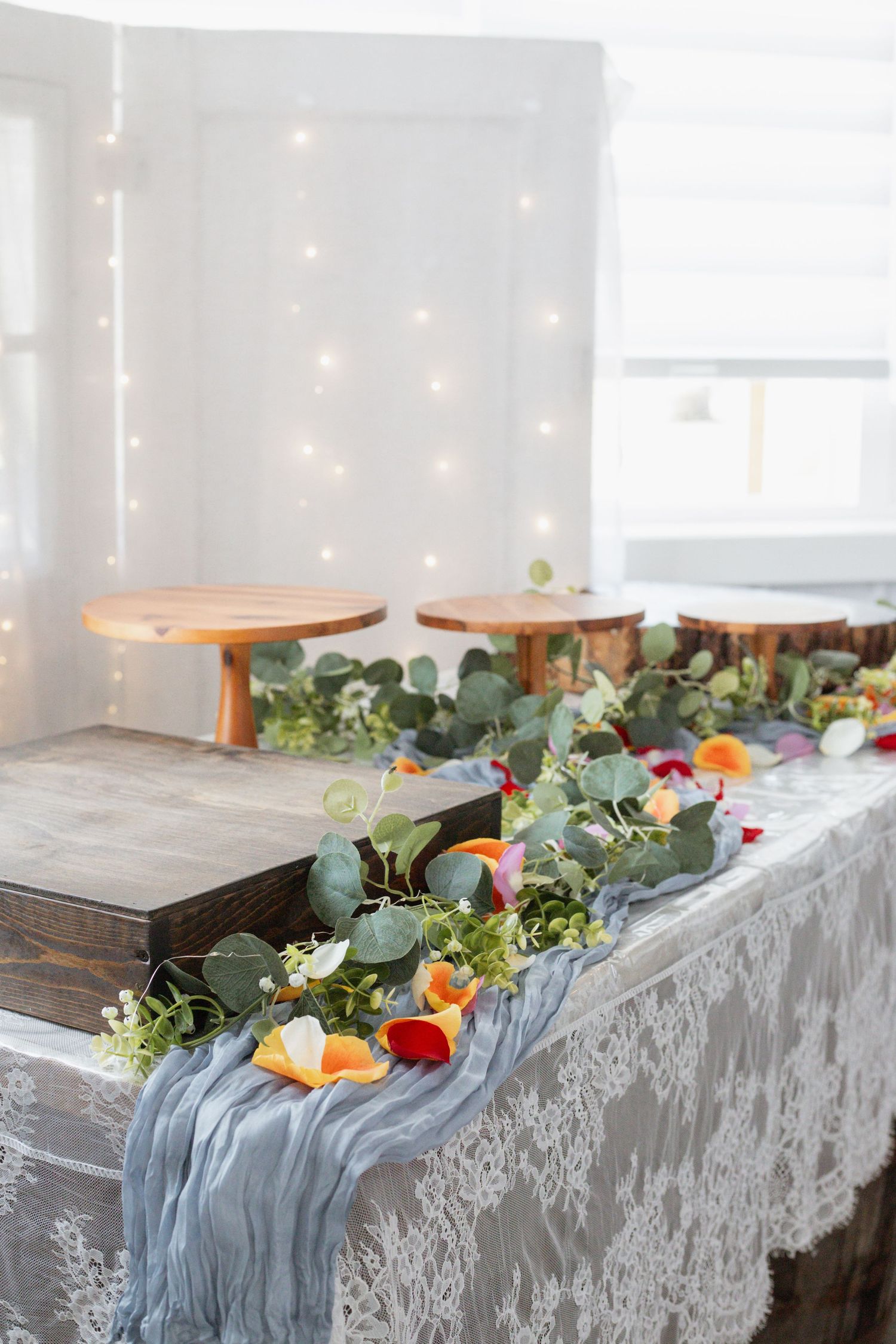 Wedding head table decorated with eucalyptus, flowers and blue runner against fairy light backdrop.