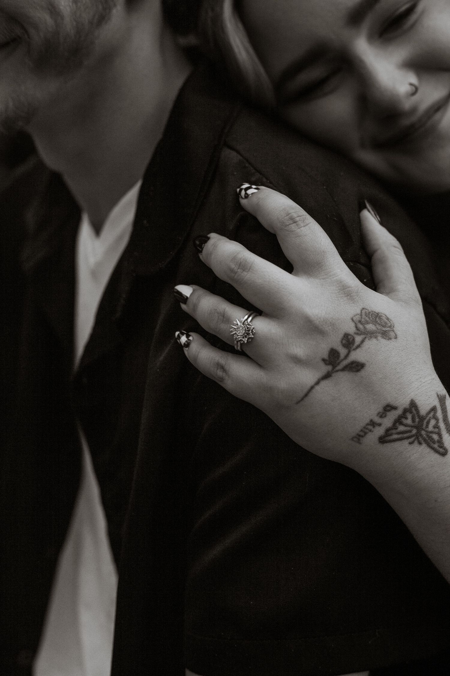Close-up of hands with tattoos and wedding rings in black and white.