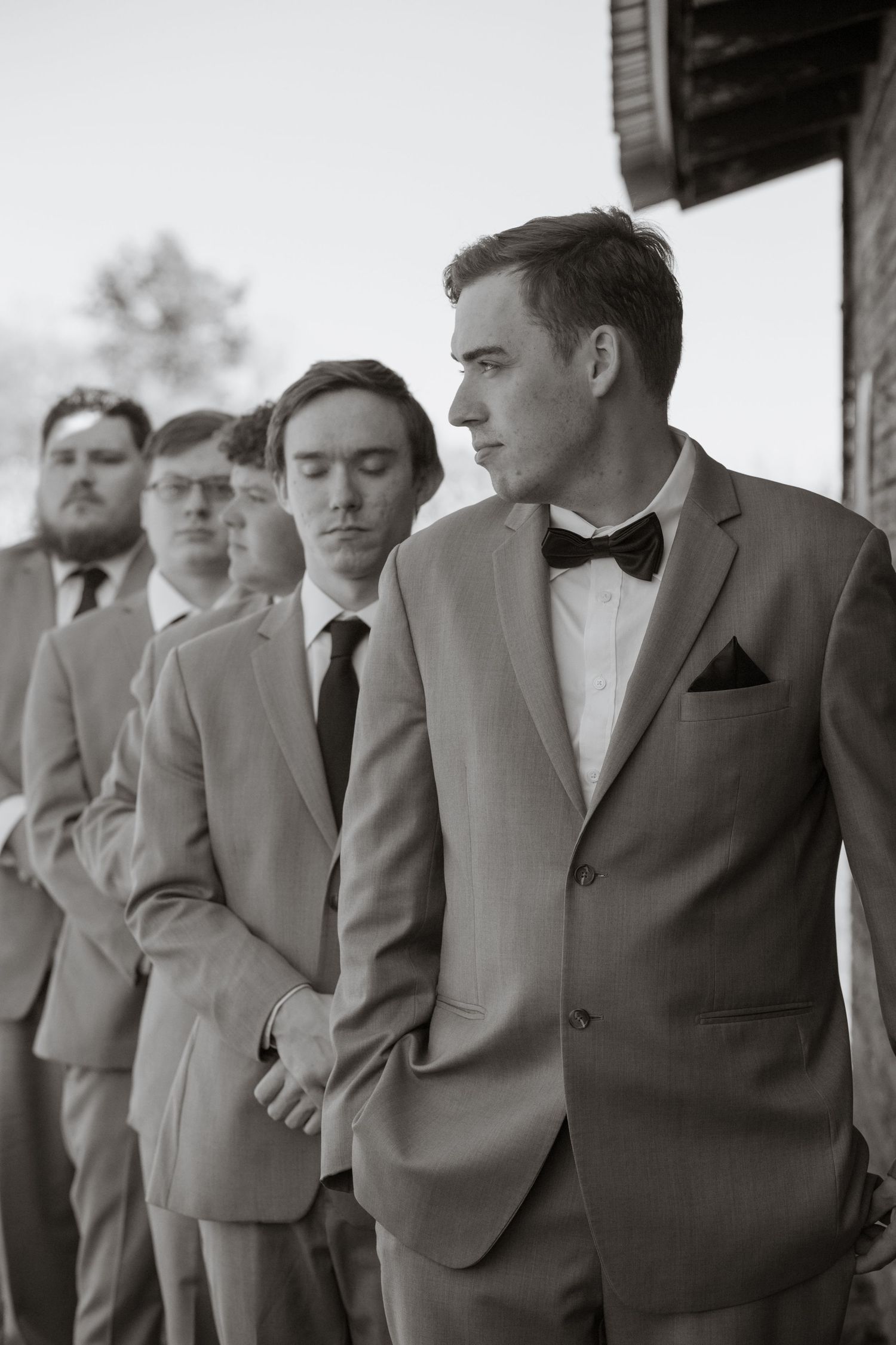 Groomsmen in formal suits and bow ties lined up during wedding ceremony.