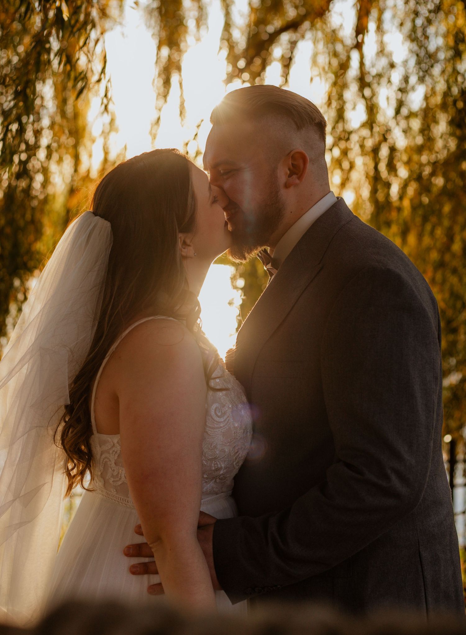 Sunset wedding portrait with golden light filtering through willow trees.
