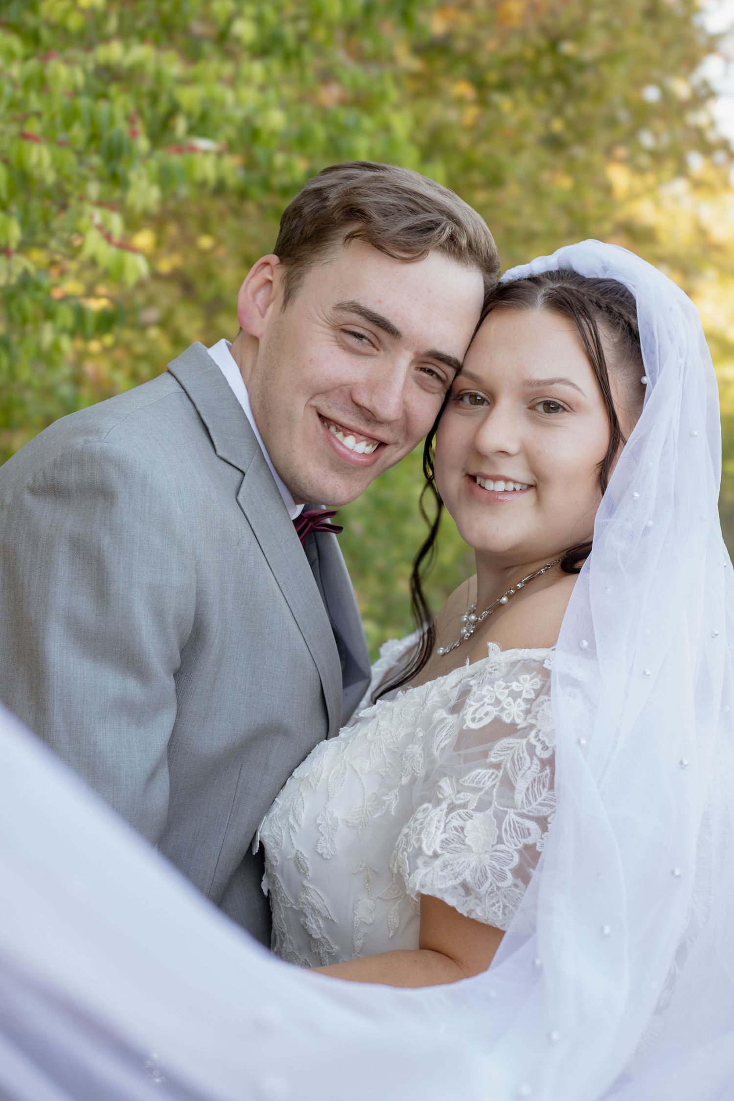 Wedding couple in gray suit and white lace dress photographed through flowing veil.