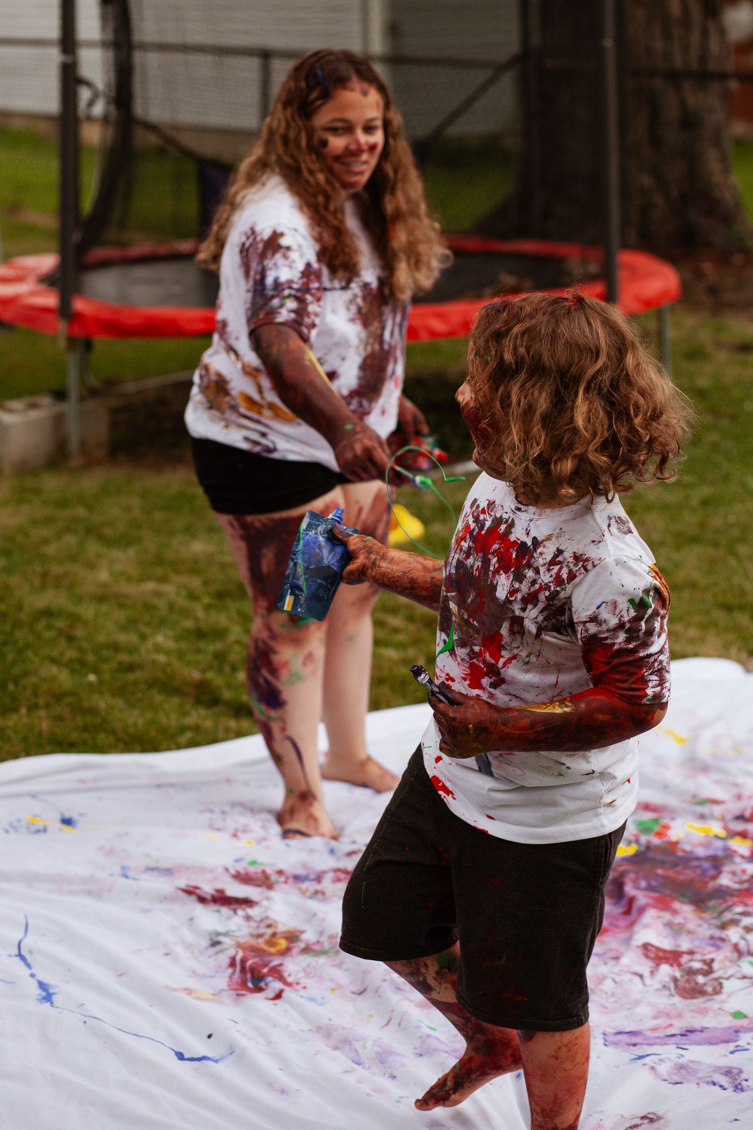 People enjoying messy paint play outdoors on large white canvas.