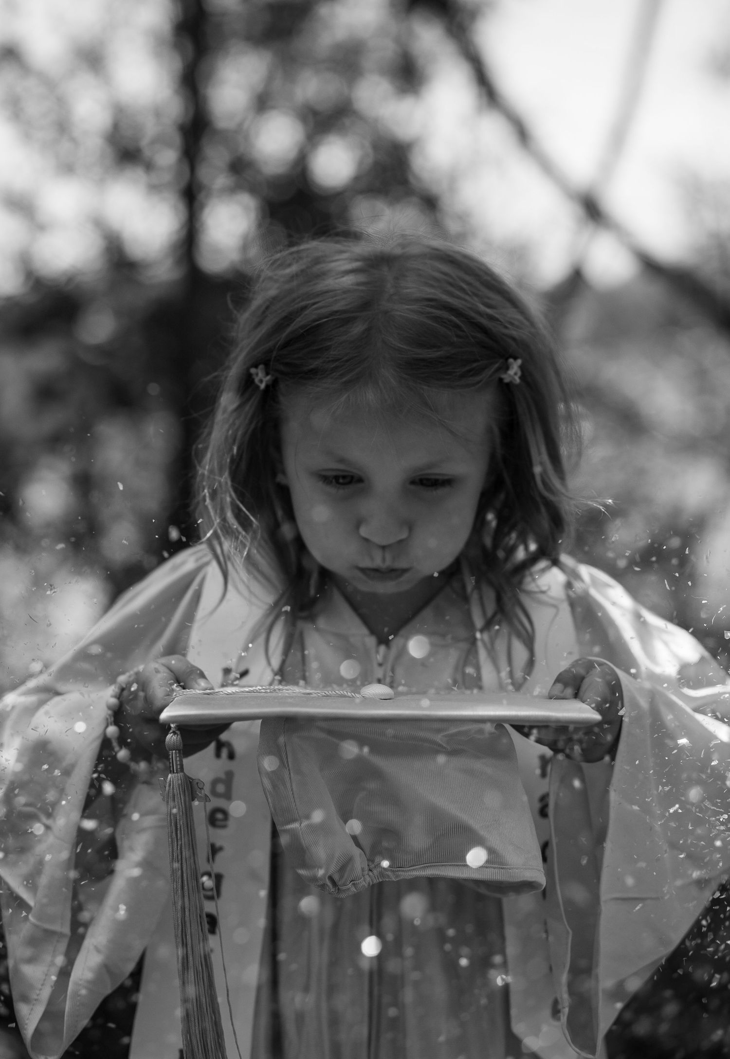 Black and white portrait of a child blowing glitter or sparkles in magical lighting.