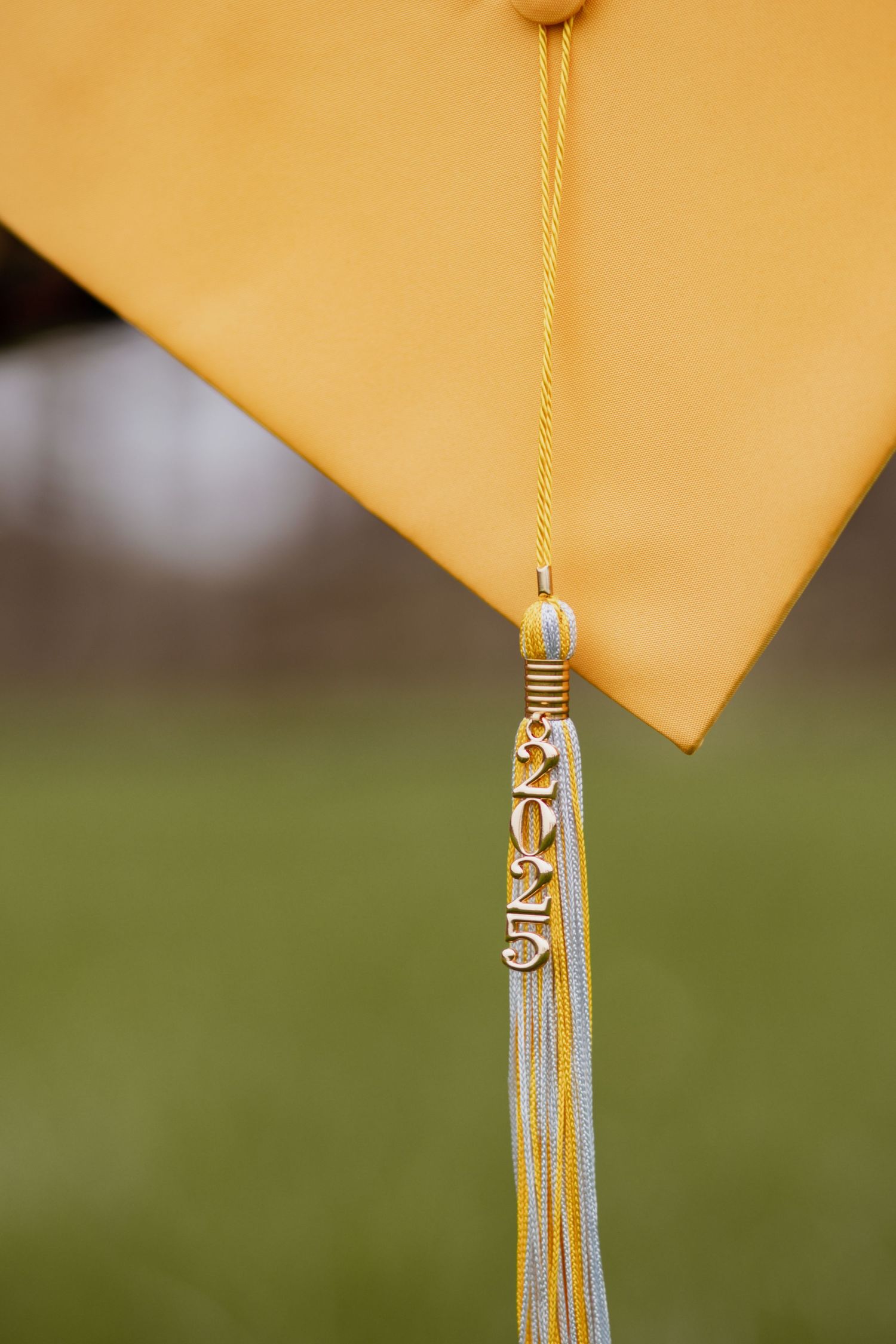 Gold graduation cap tassel with silver accents against yellow background.