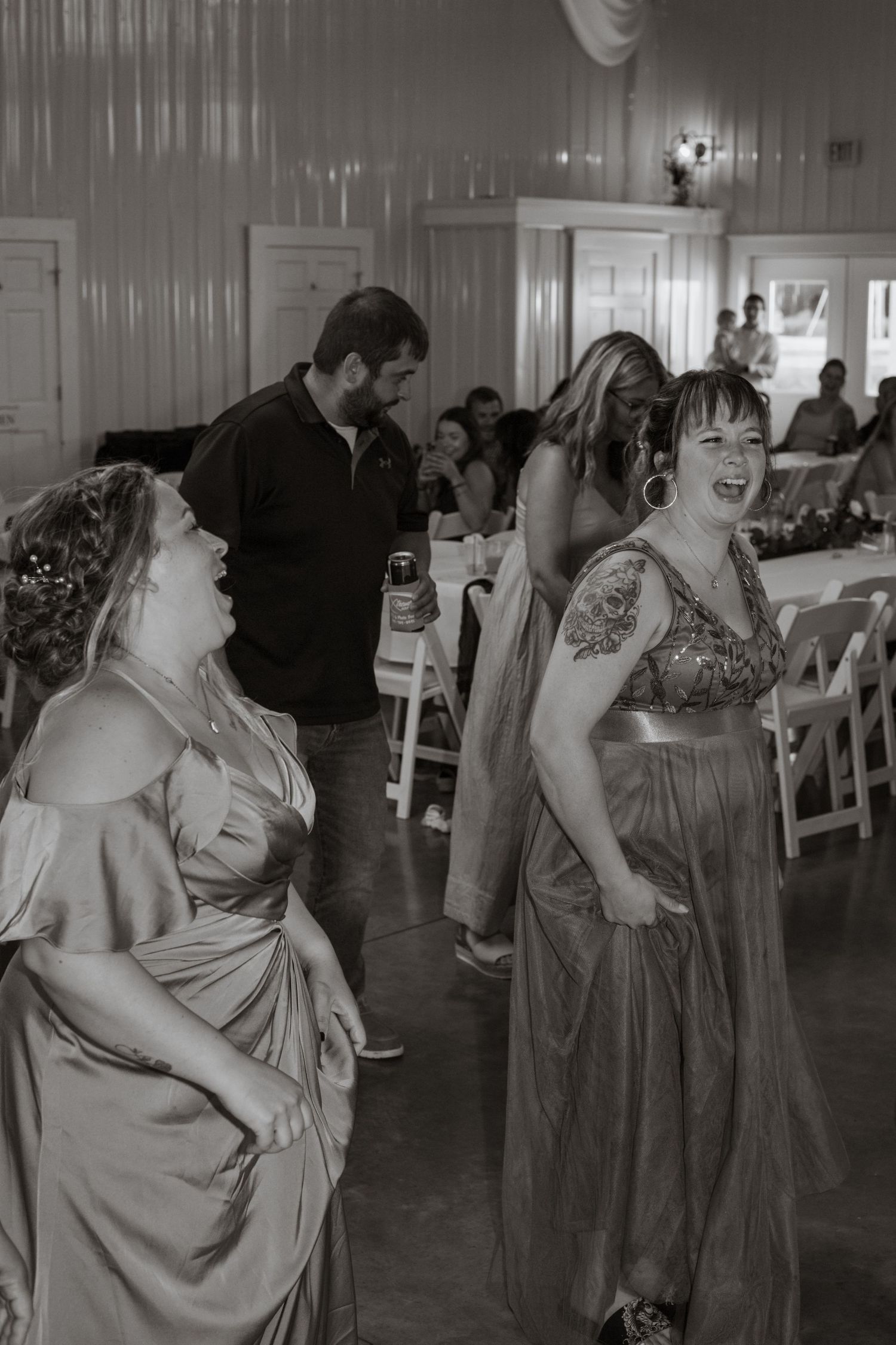 Wedding guests in formal attire dancing and laughing at a reception in black and white.