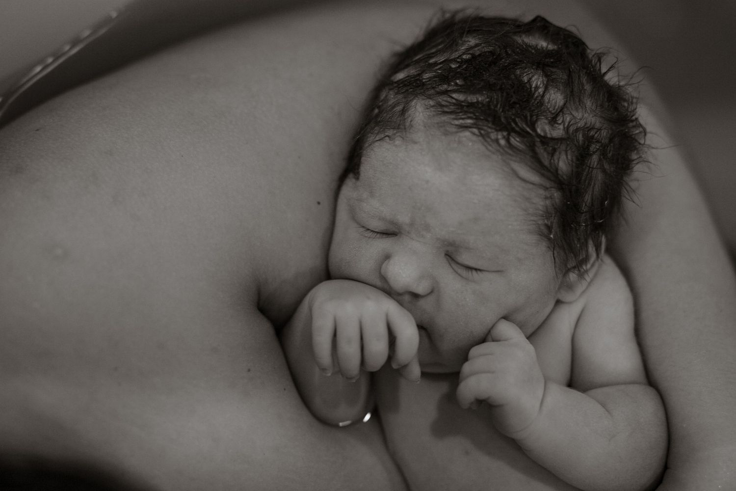 A peaceful black and white portrait of a sleeping newborn baby with tiny fingers curled near their face.