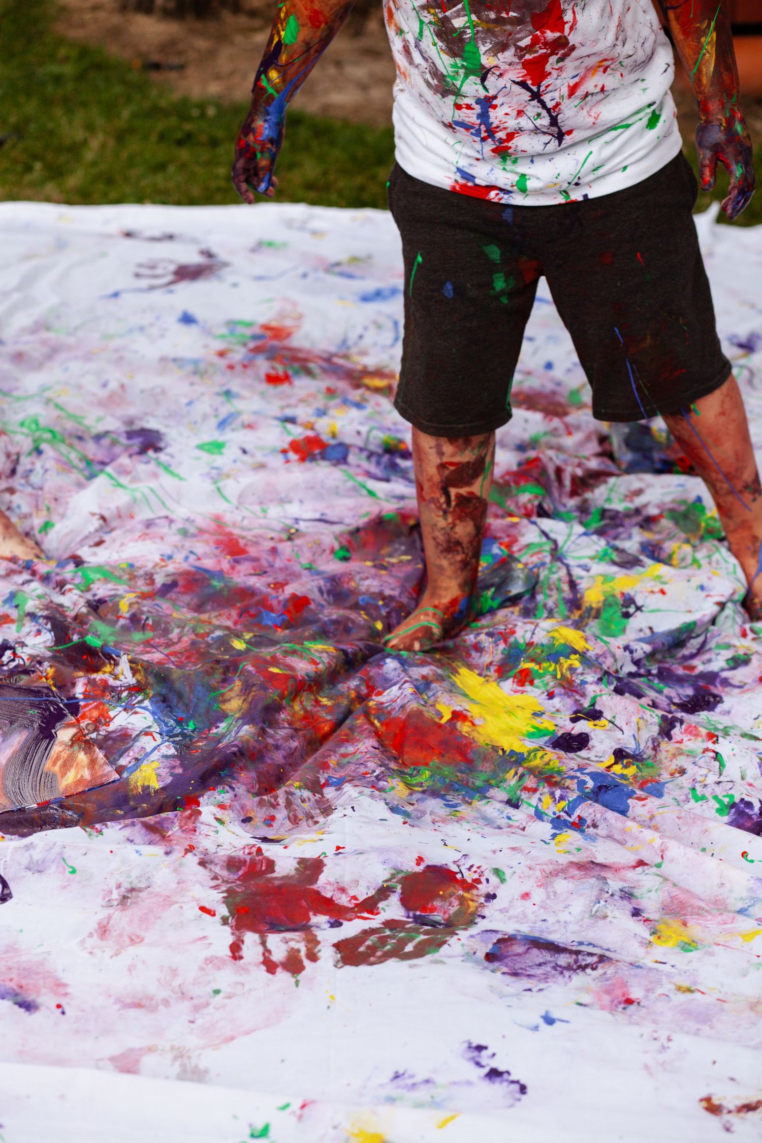 Colorful paint footprints and handprints create abstract patterns on white canvas.