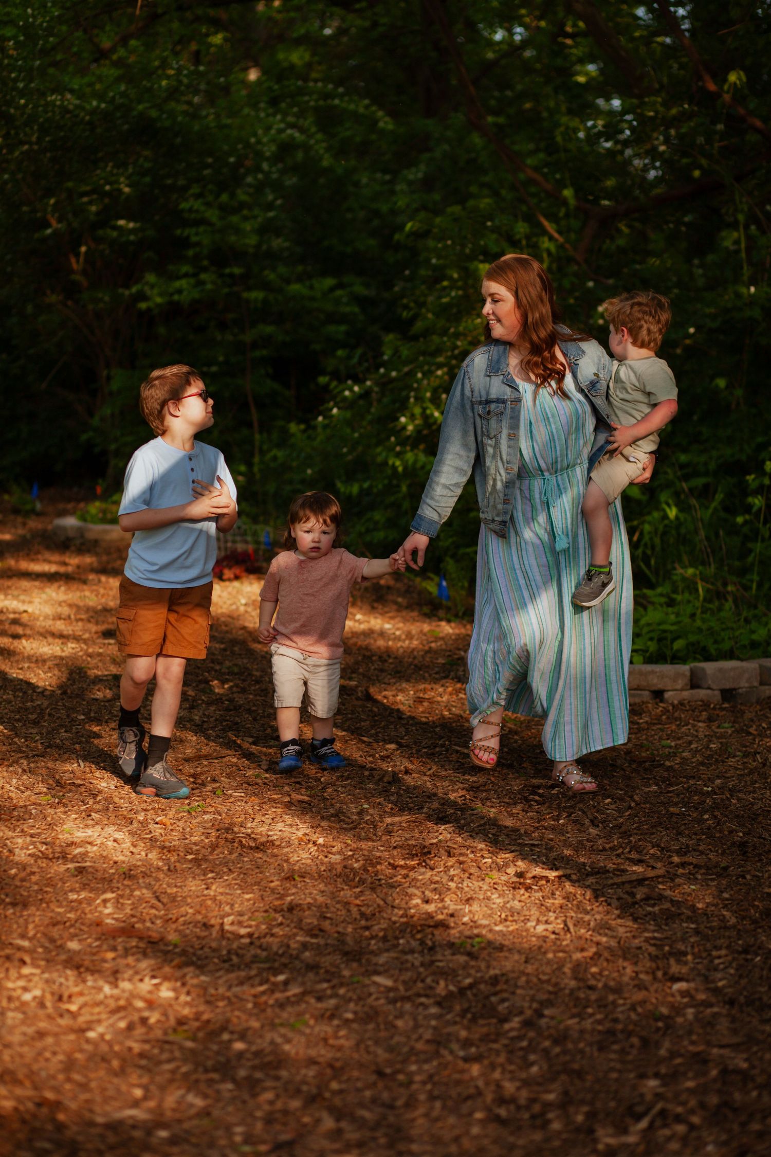 A family walking together through a sunlit wooded area in casual clothing.
