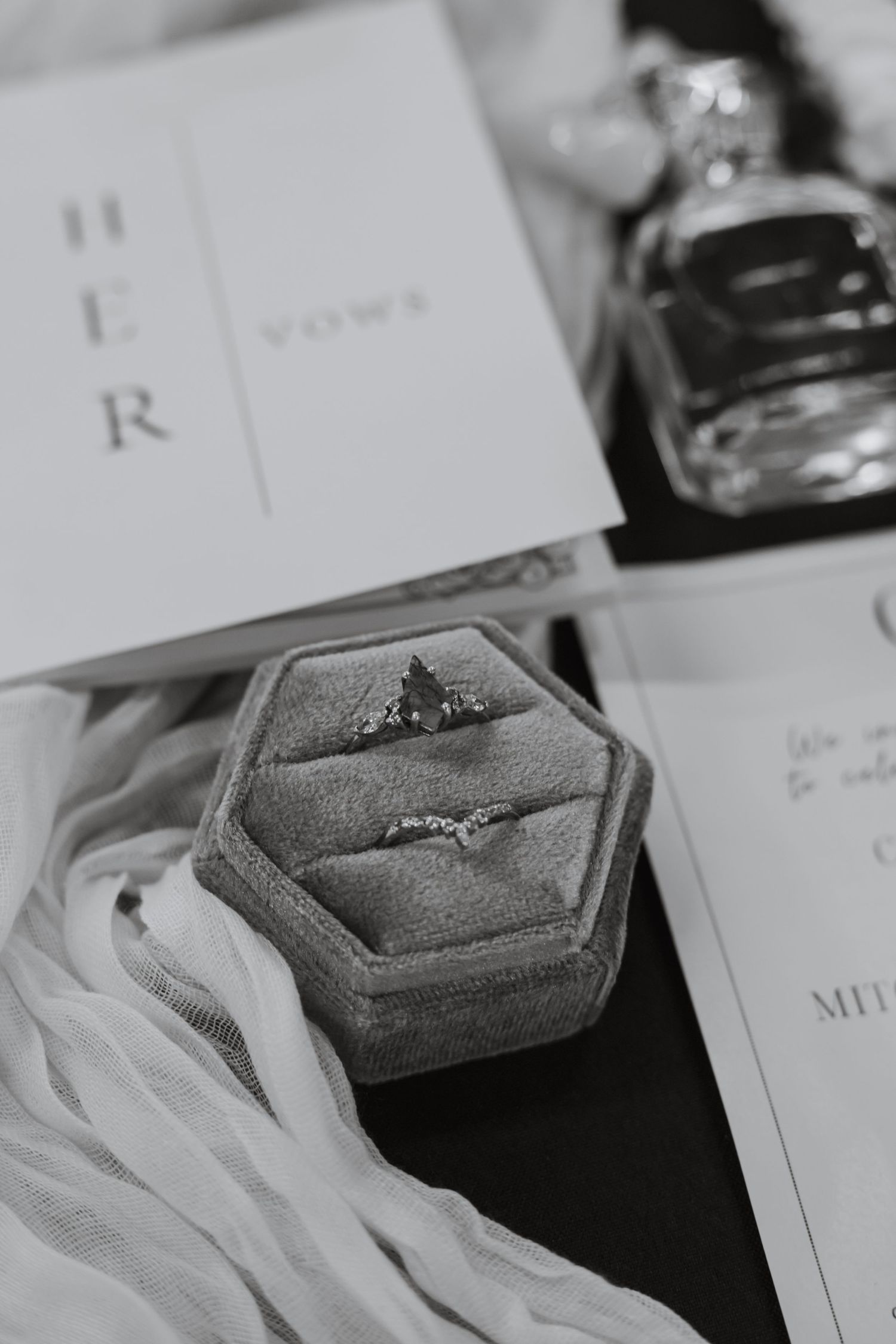 A gray velvet ring box containing an engagement ring photographed with wedding stationery.