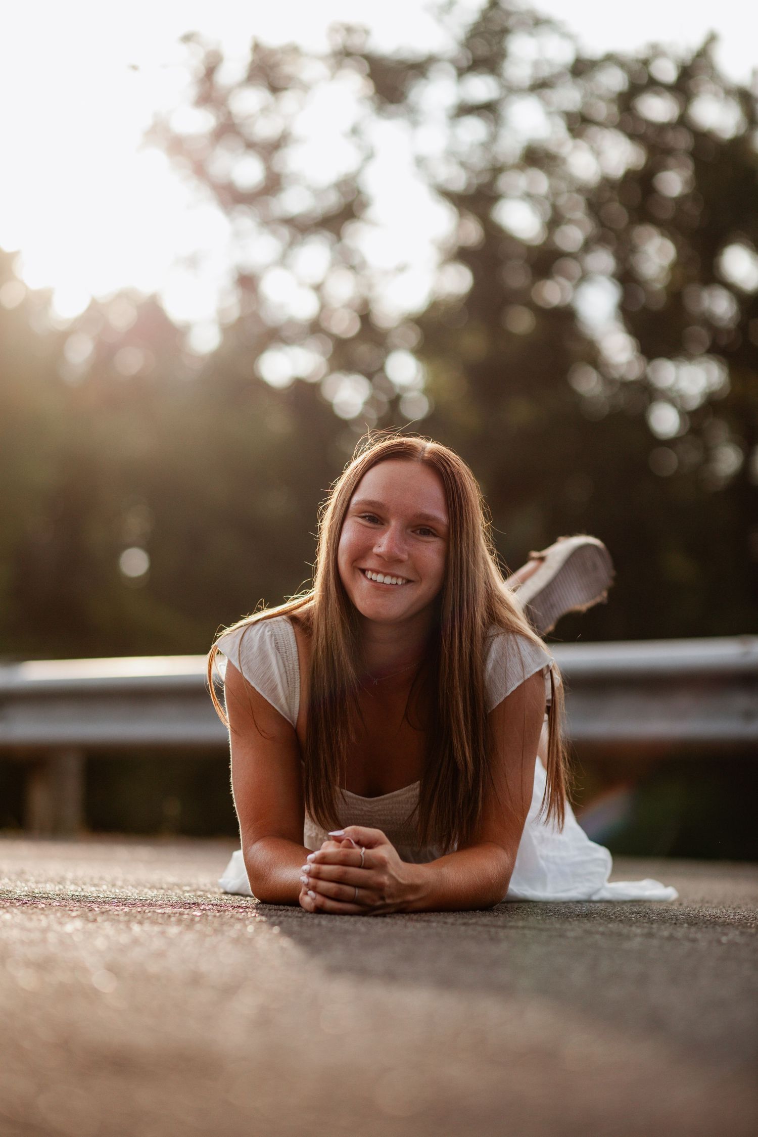 Person in casual attire lying on pavement during golden hour photography session.