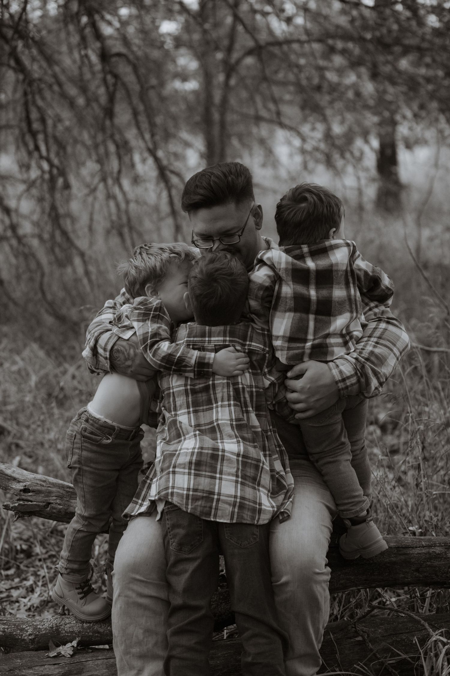 Black and white photo of family members embracing on a fallen tree in nature.
