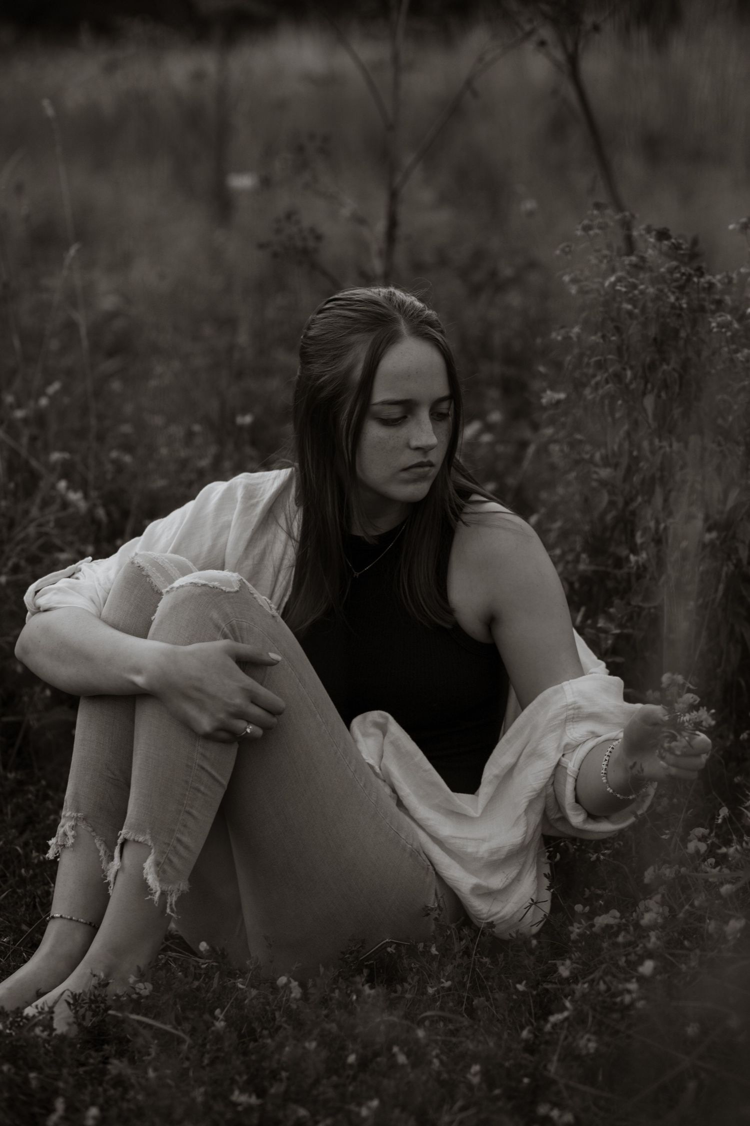 Moody black and white portrait of someone reclining among flowers in a white dress.