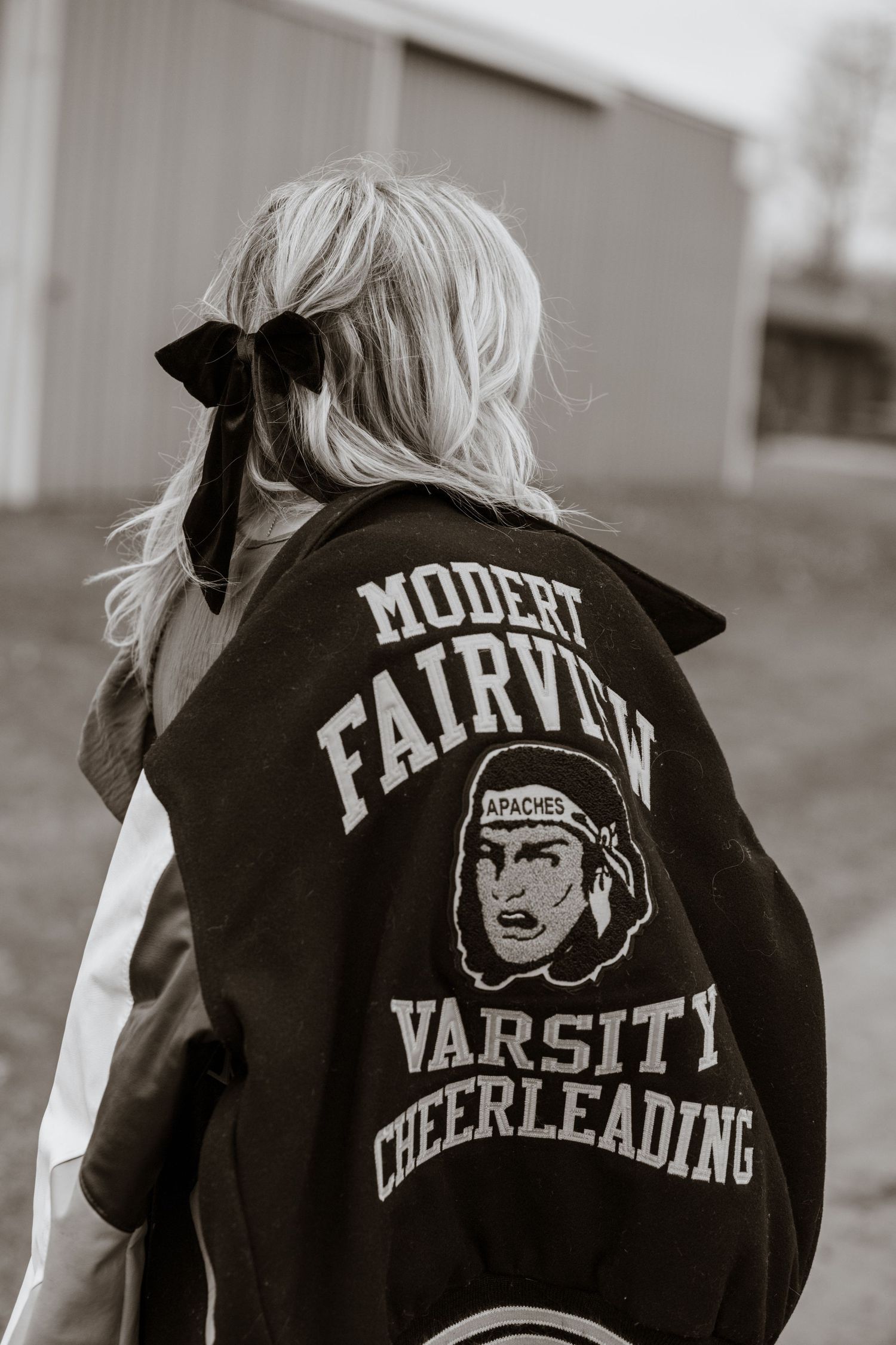Black and white photos showing the back of a varsity cheerleading jacket with lettering and logos.