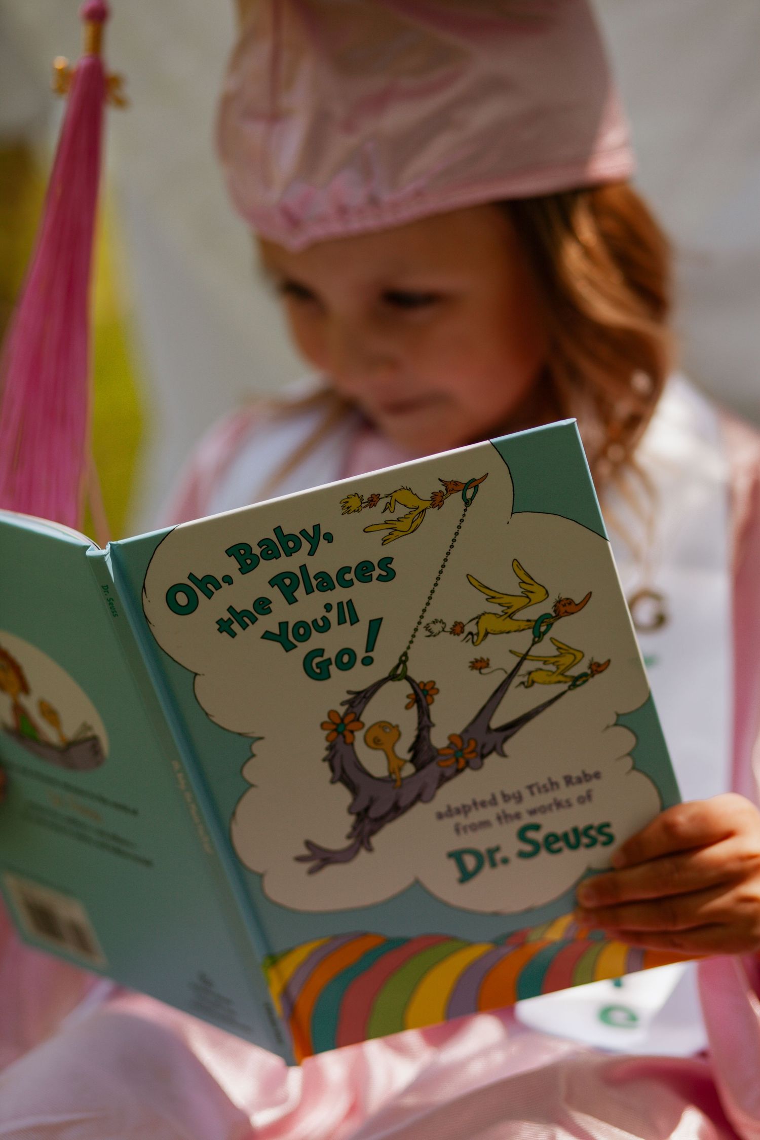 Someone reading the Dr. Seuss book 'Oh, The Places You'll Go!' while wearing pink clothing.