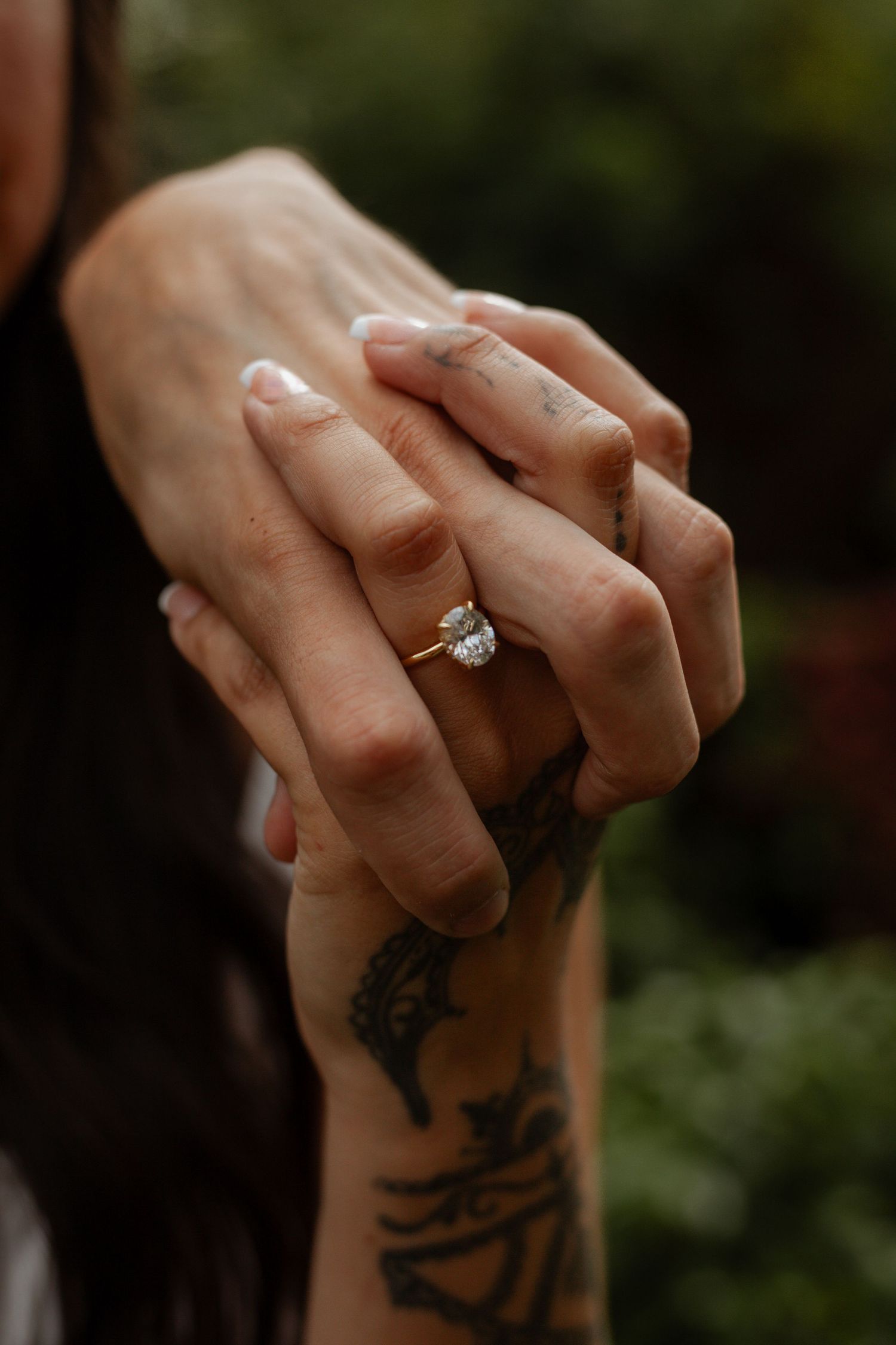 Close-up of hands with engagement ring and delicate tattoo details.