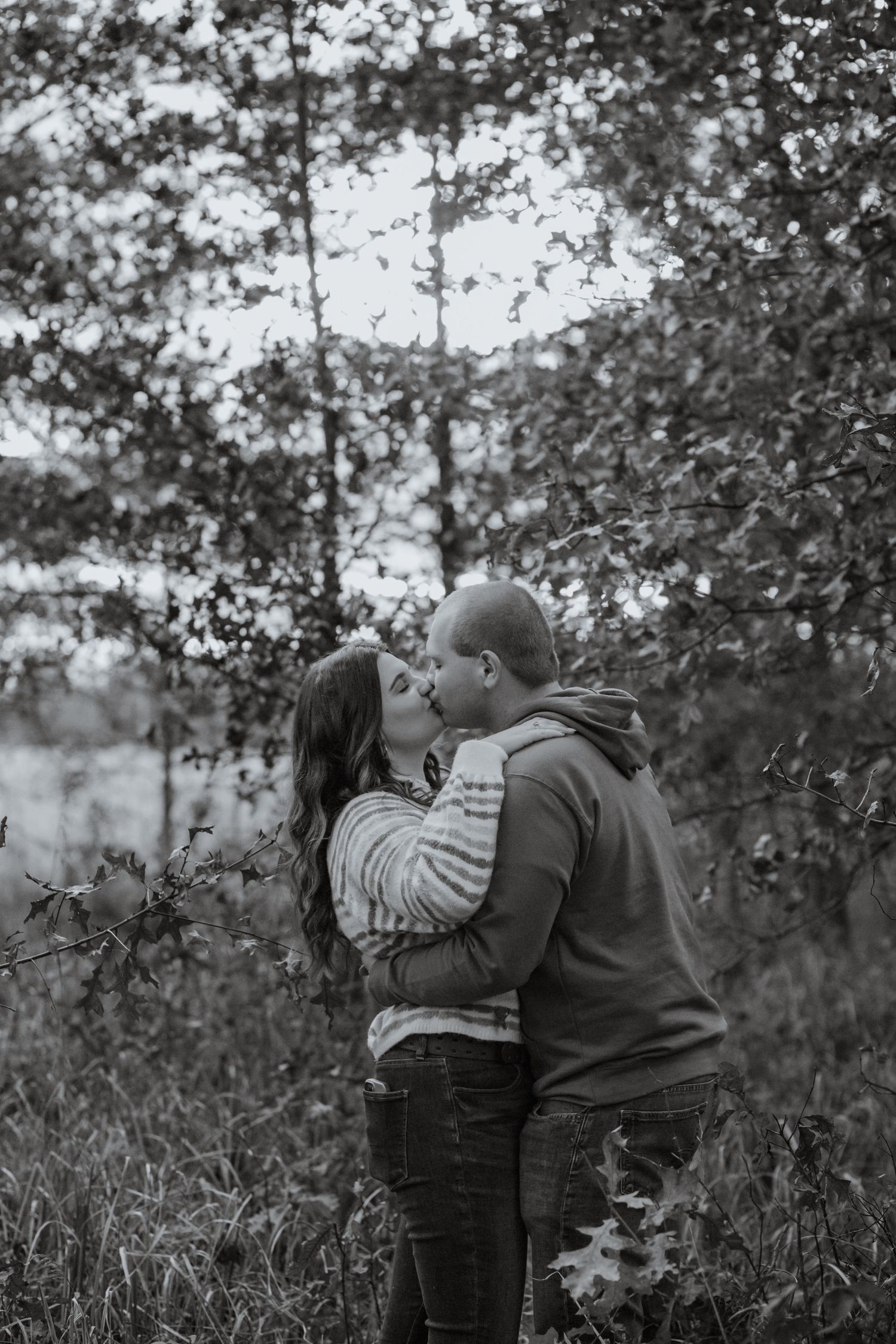 A romantic couple sharing an intimate kiss among autumn trees in a natural outdoor setting.