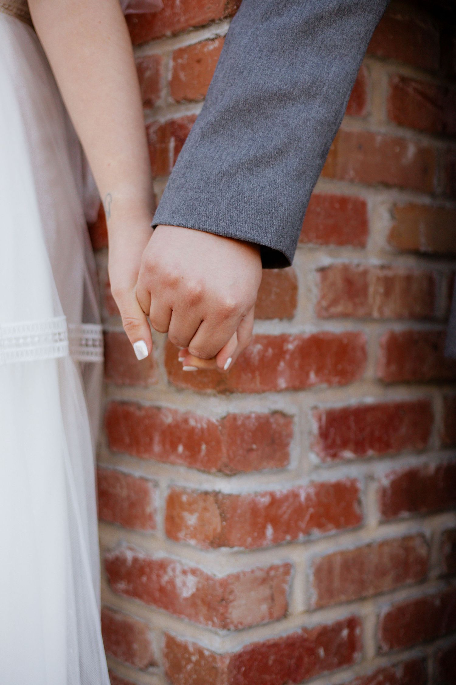 Wedding detail shots of hands and formal attire against rustic brick background.