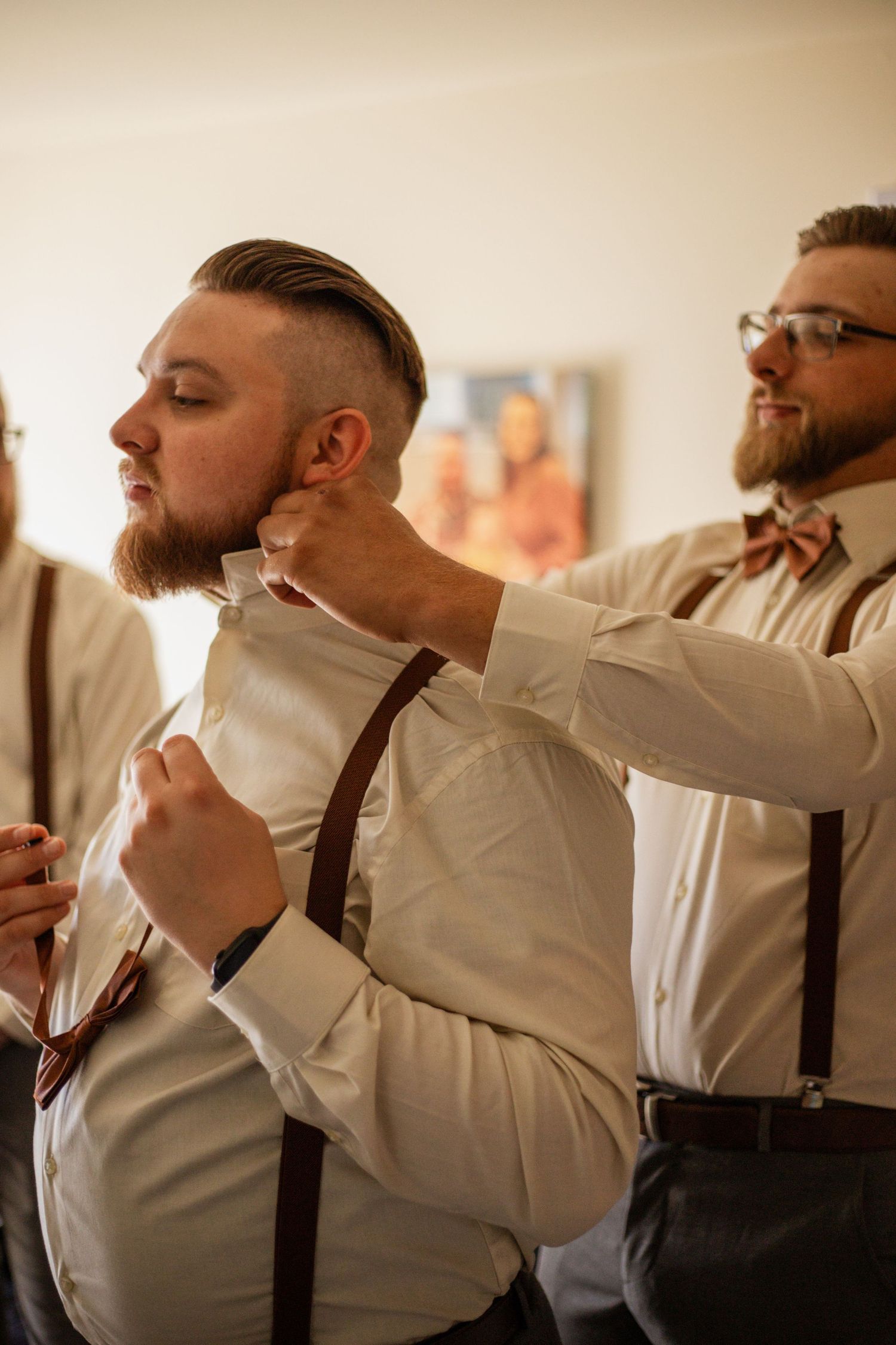 Groomsmen in white shirts and suspenders adjusting their ties before the ceremony.