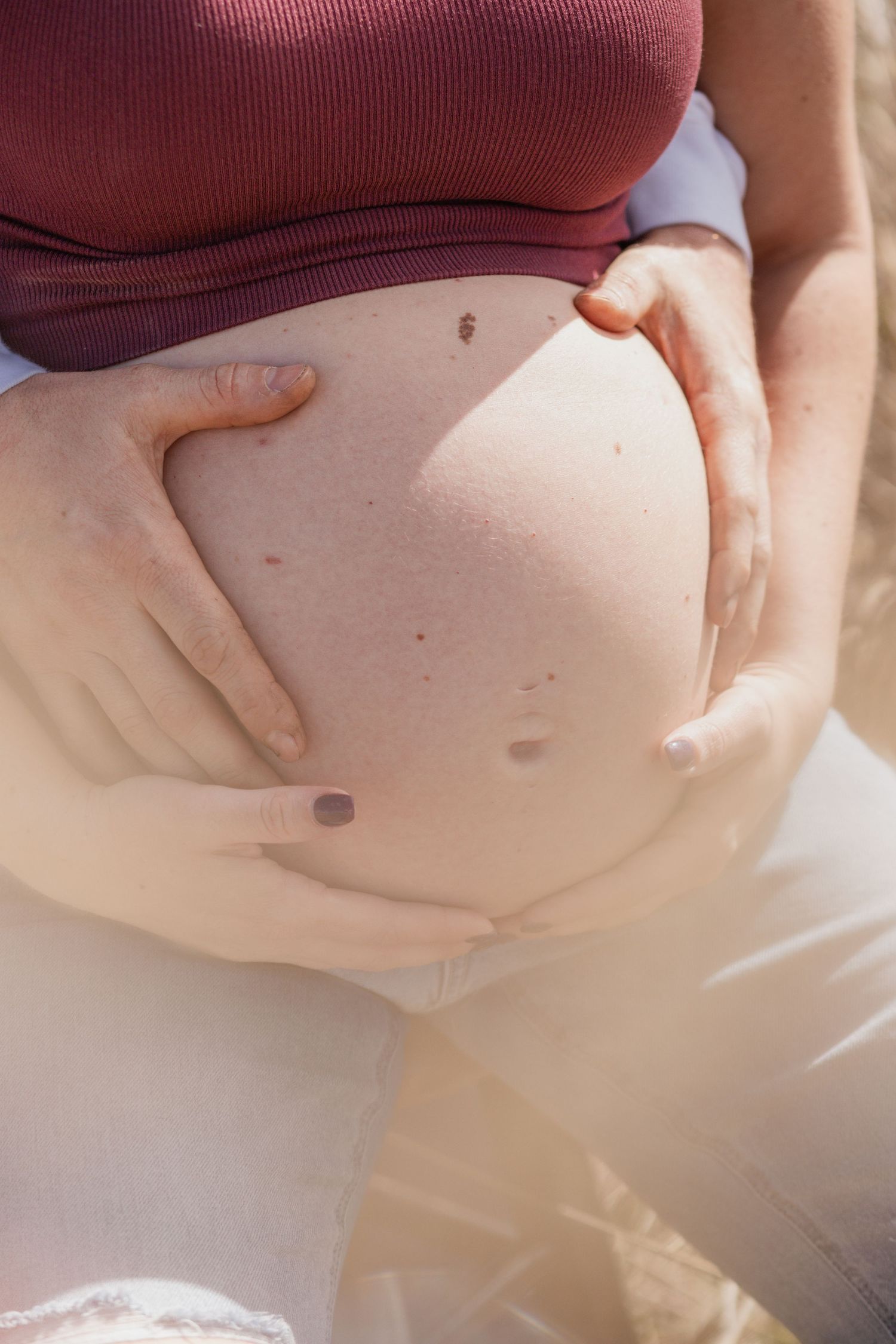 Close-up view of hands gently cradling a pregnant belly in natural lighting.