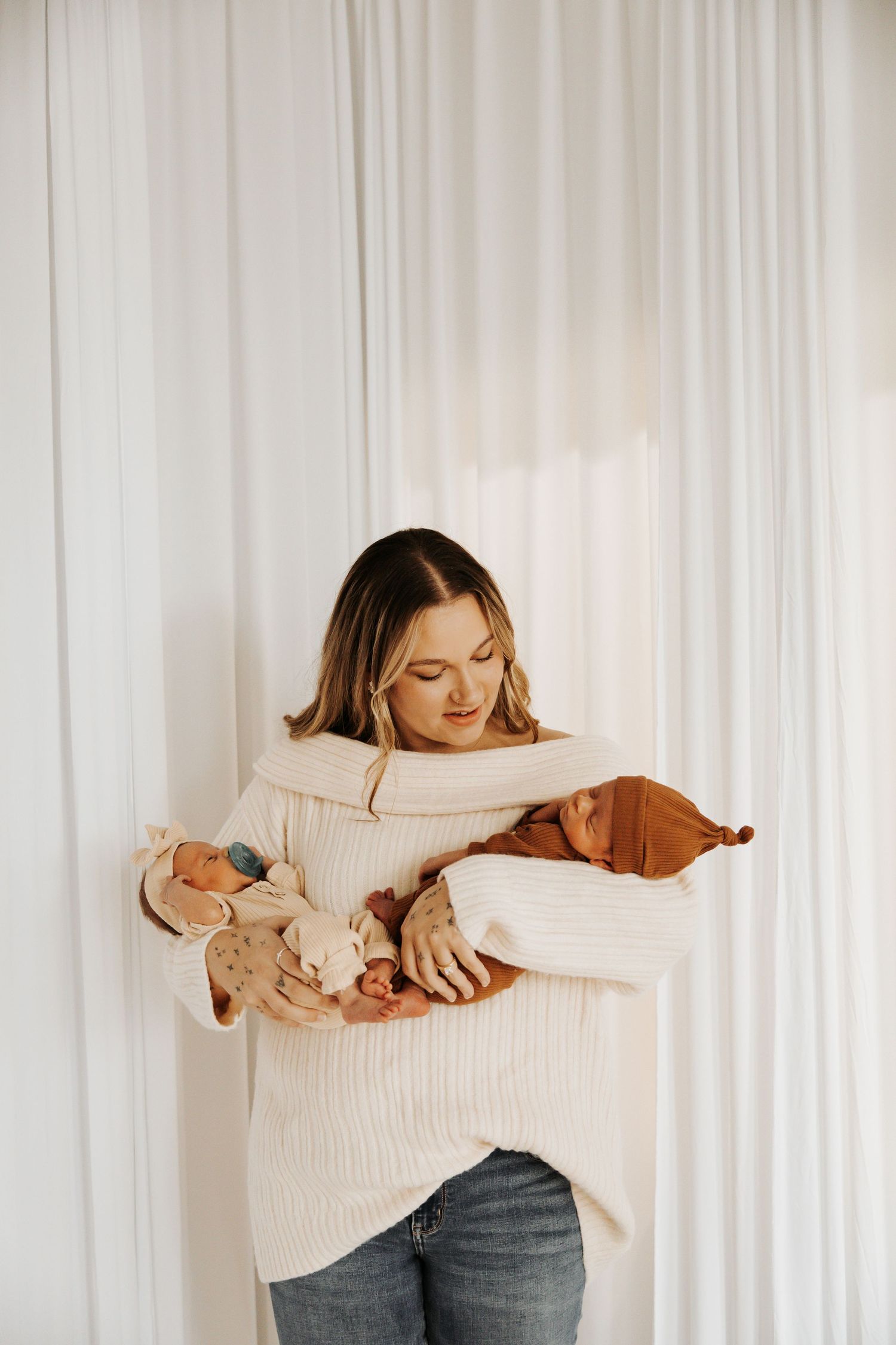 Woman in cream sweater holding small sleeping puppy against white curtain background.