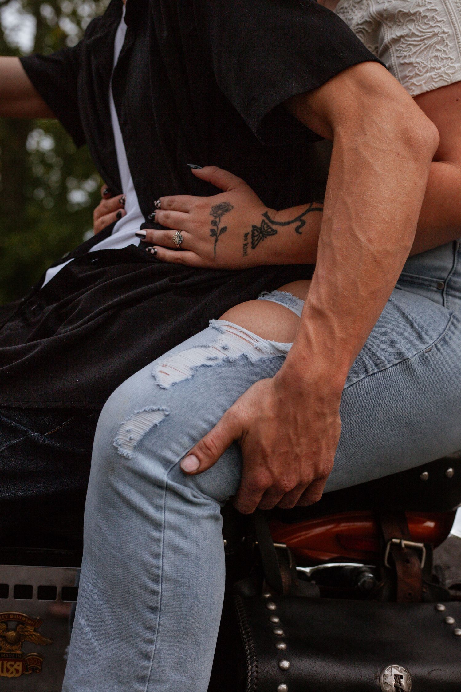 Detail shot of denim jeans and tattoos while sitting on a motorcycle.