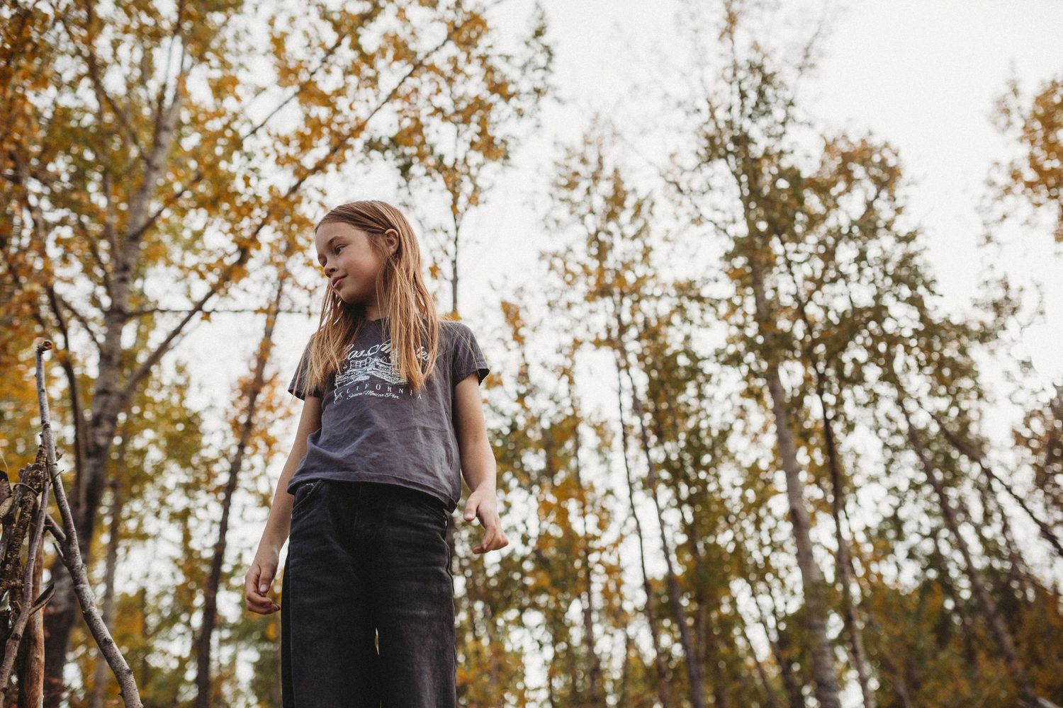 Girl standing in fall trees in a documentary style Calgary family photography session in Prince's Island Park
