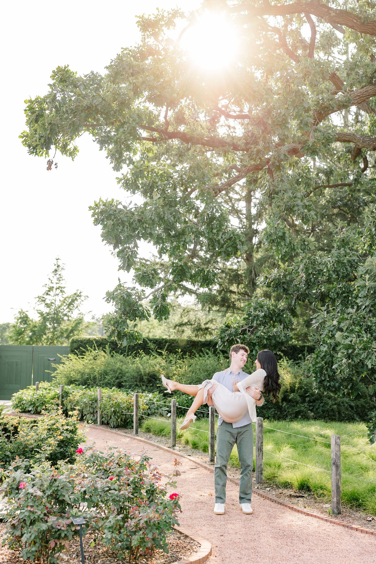 Jack carries Alysia through the gardens as sunlight glows through the trees at Cantigny Park.