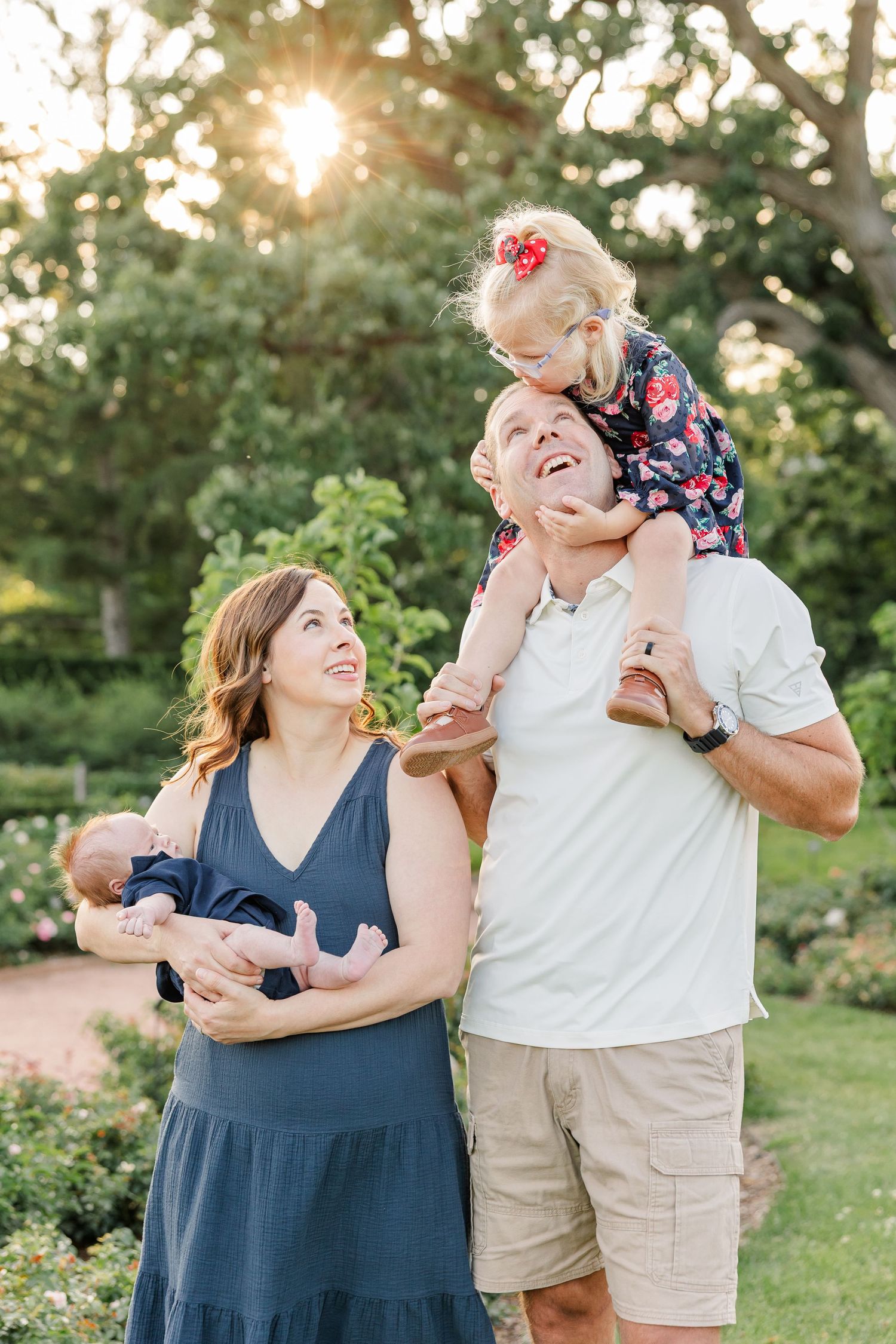 Hilary and Andrew smiling at Caroline while she sits on her dad’s shoulders beside baby Lincoln.