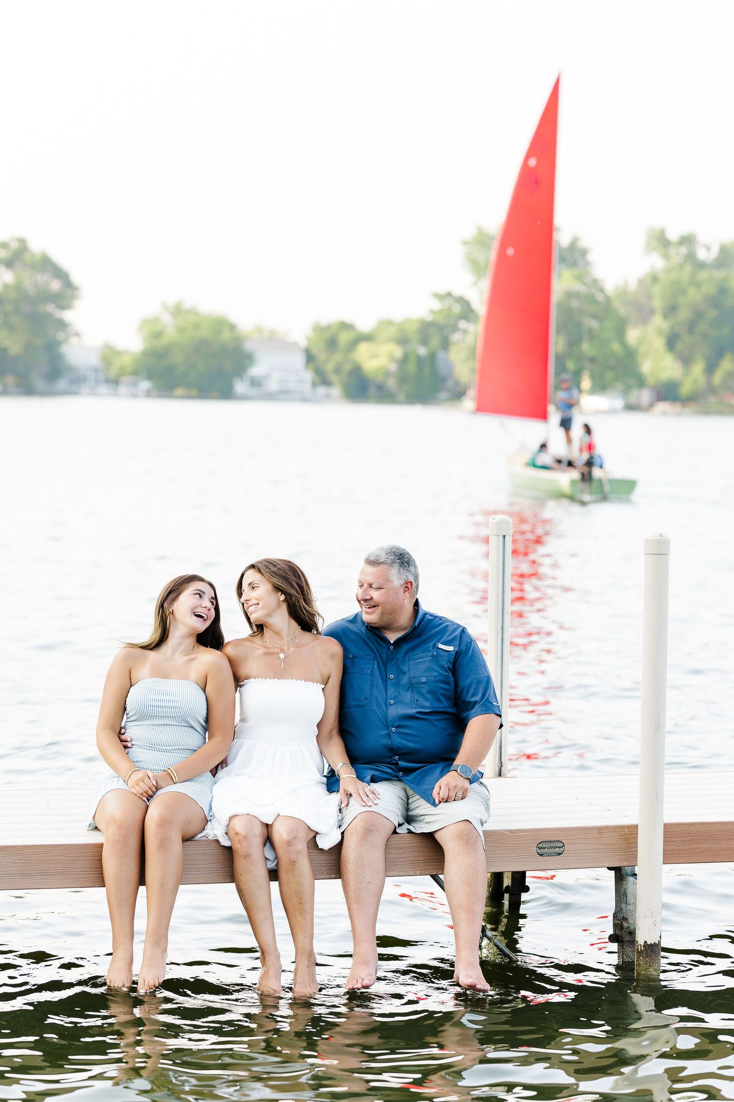 Family sitting on dock with red sailboat during Pistakee Lake family photos