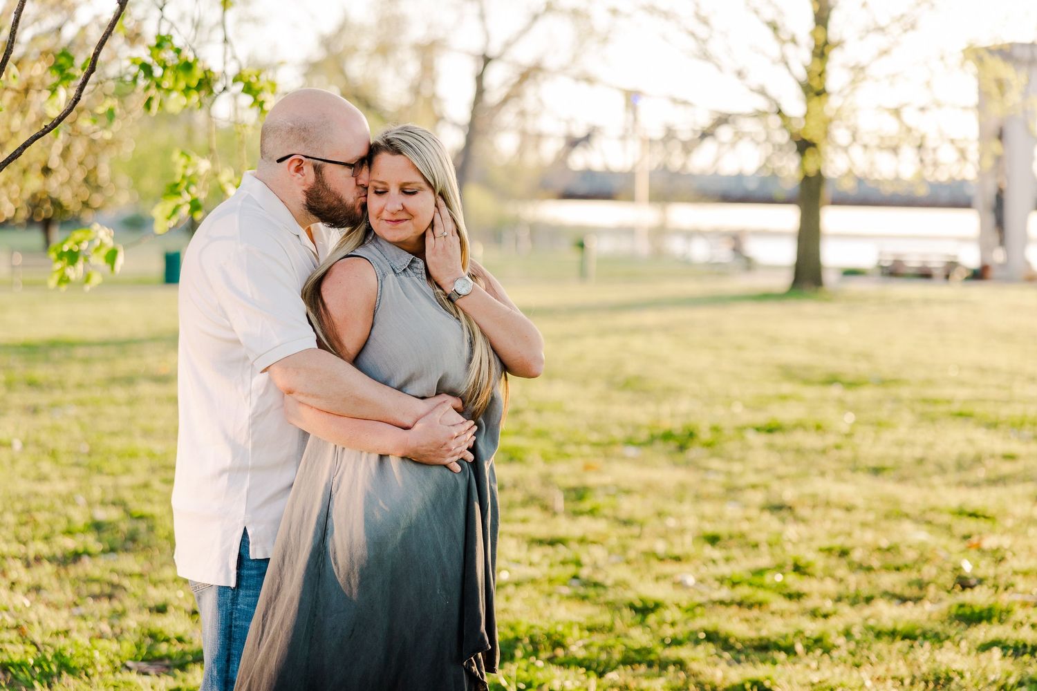 A tender moment captured between a couple embracing in a sunlit park setting.