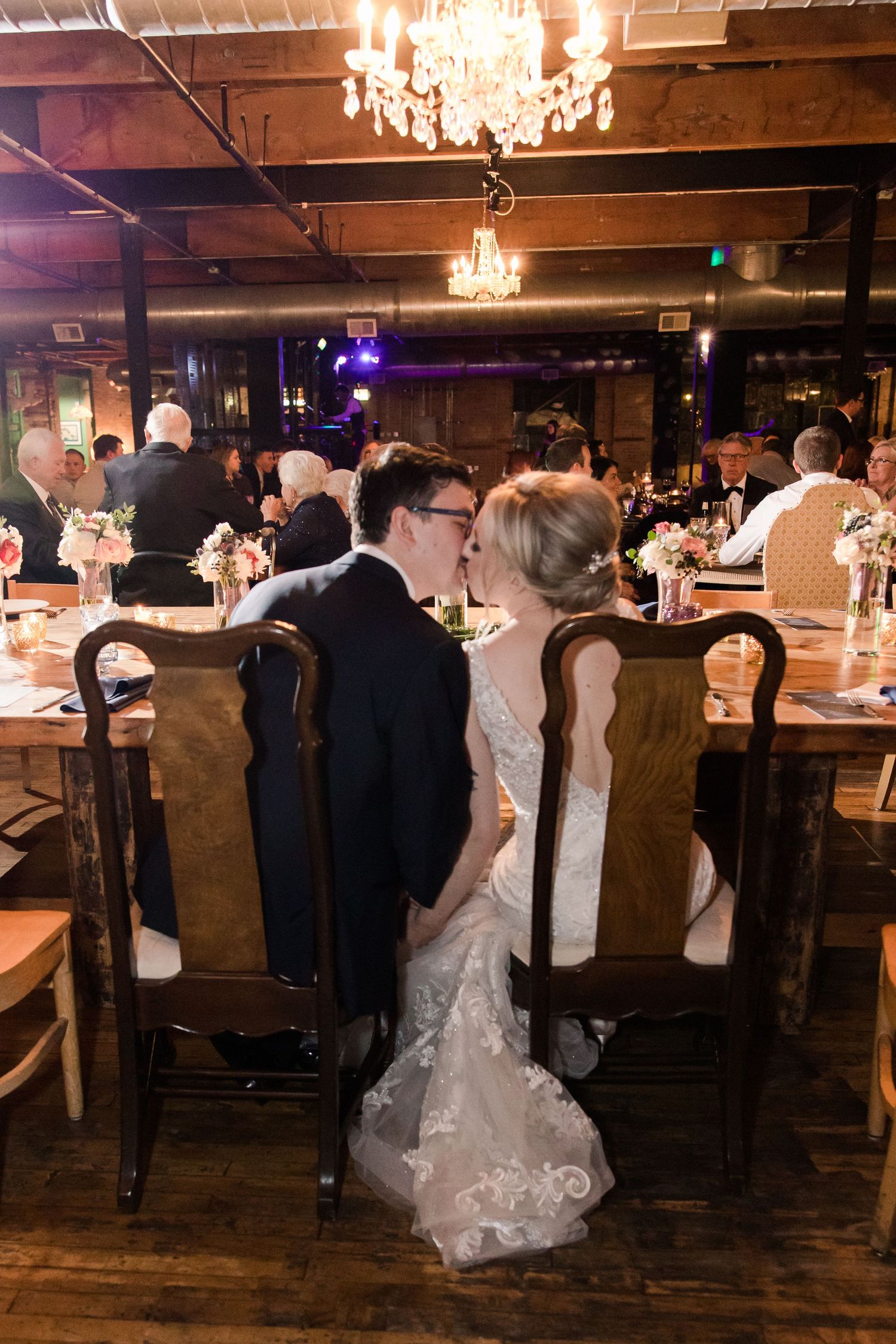 Wedding reception in rustic venue with crystal chandeliers and wooden decor.