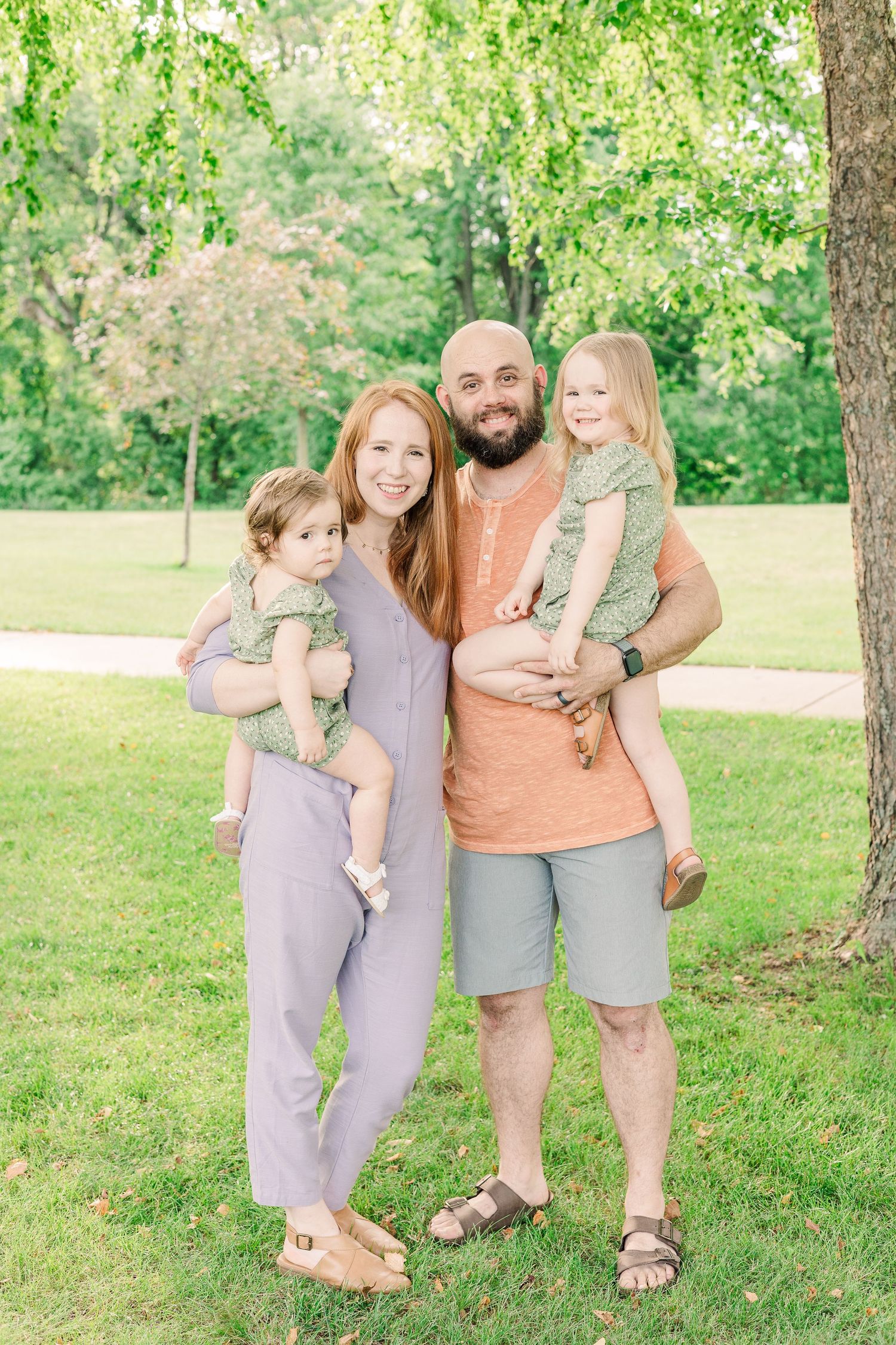 A family of four poses together outdoors on a sunny day in casual attire.