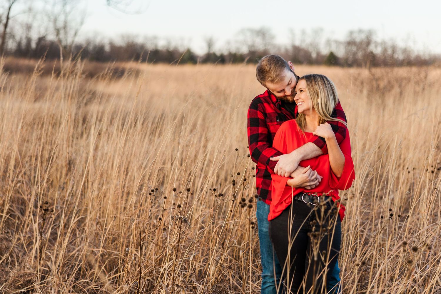 Romantic couple embracing in tall golden grass field wearing red and plaid.