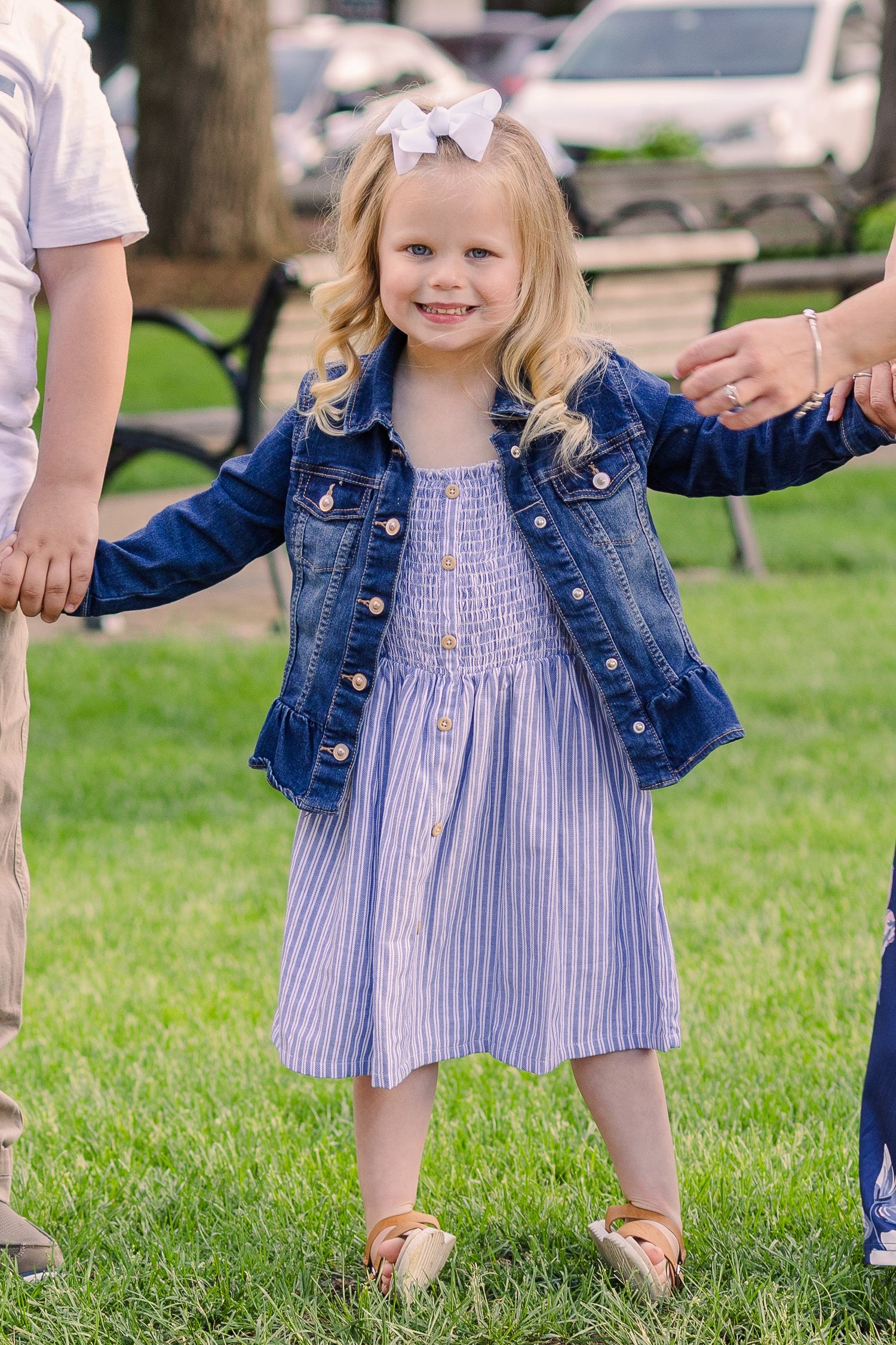 Young girl in denim jacket and striped dress stands confidently while holding hands.