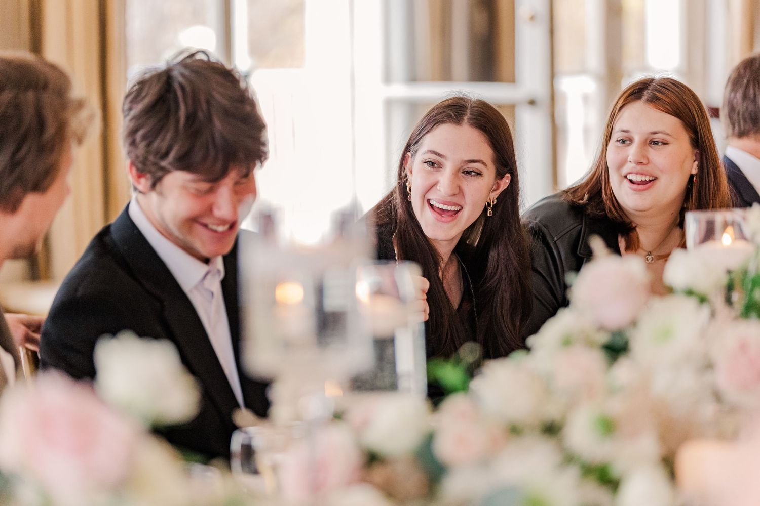 Candid moment of wedding guests laughing and socializing at reception dinner with floral decor.