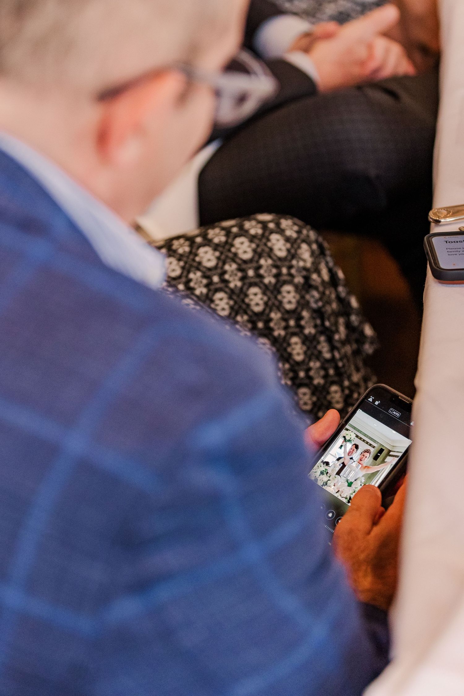 Guest in blue checked jacket looking at phone screen at elegant event.