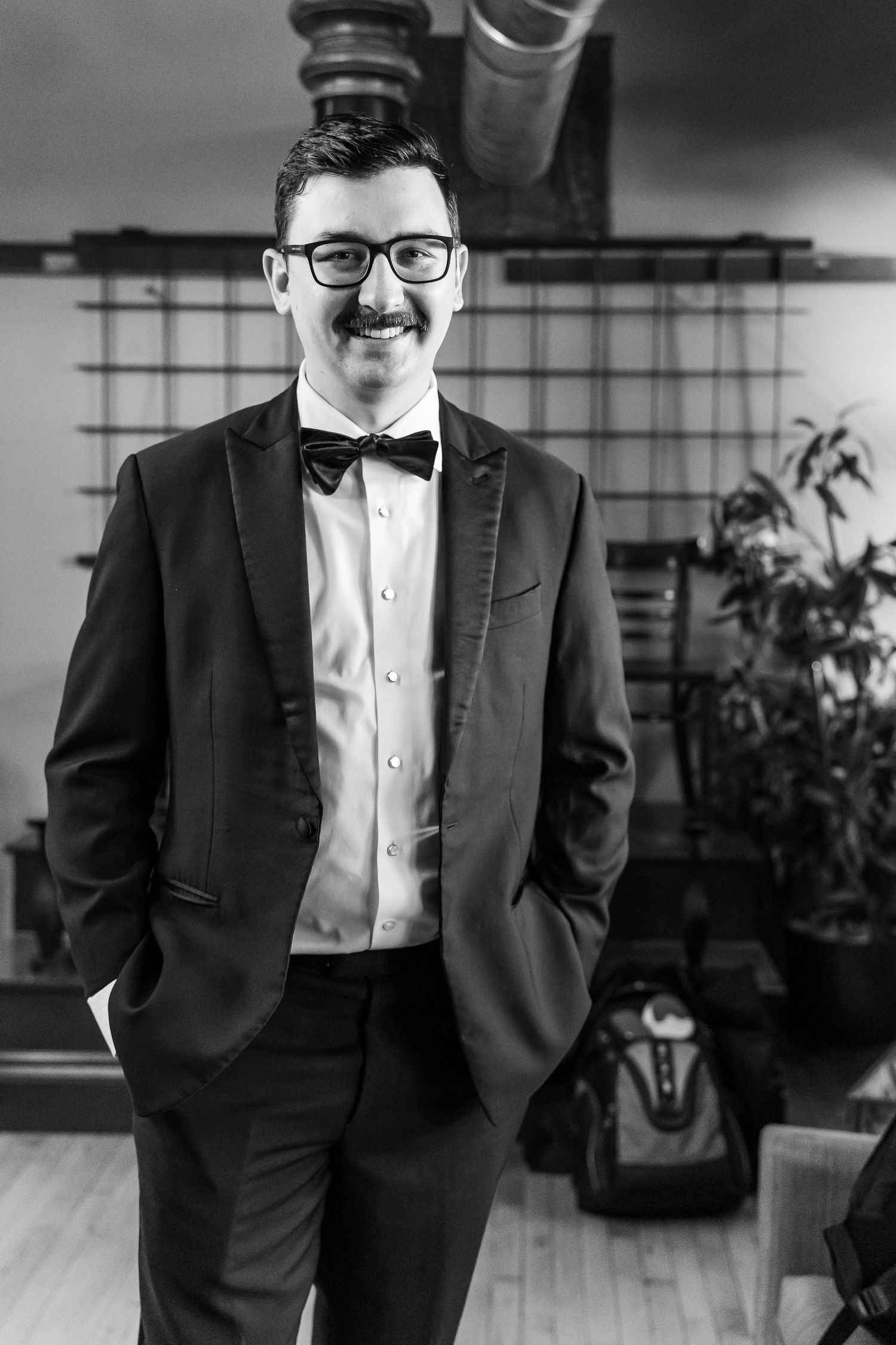 Formal portrait of a person in a tuxedo and bow tie standing with hands in pockets.