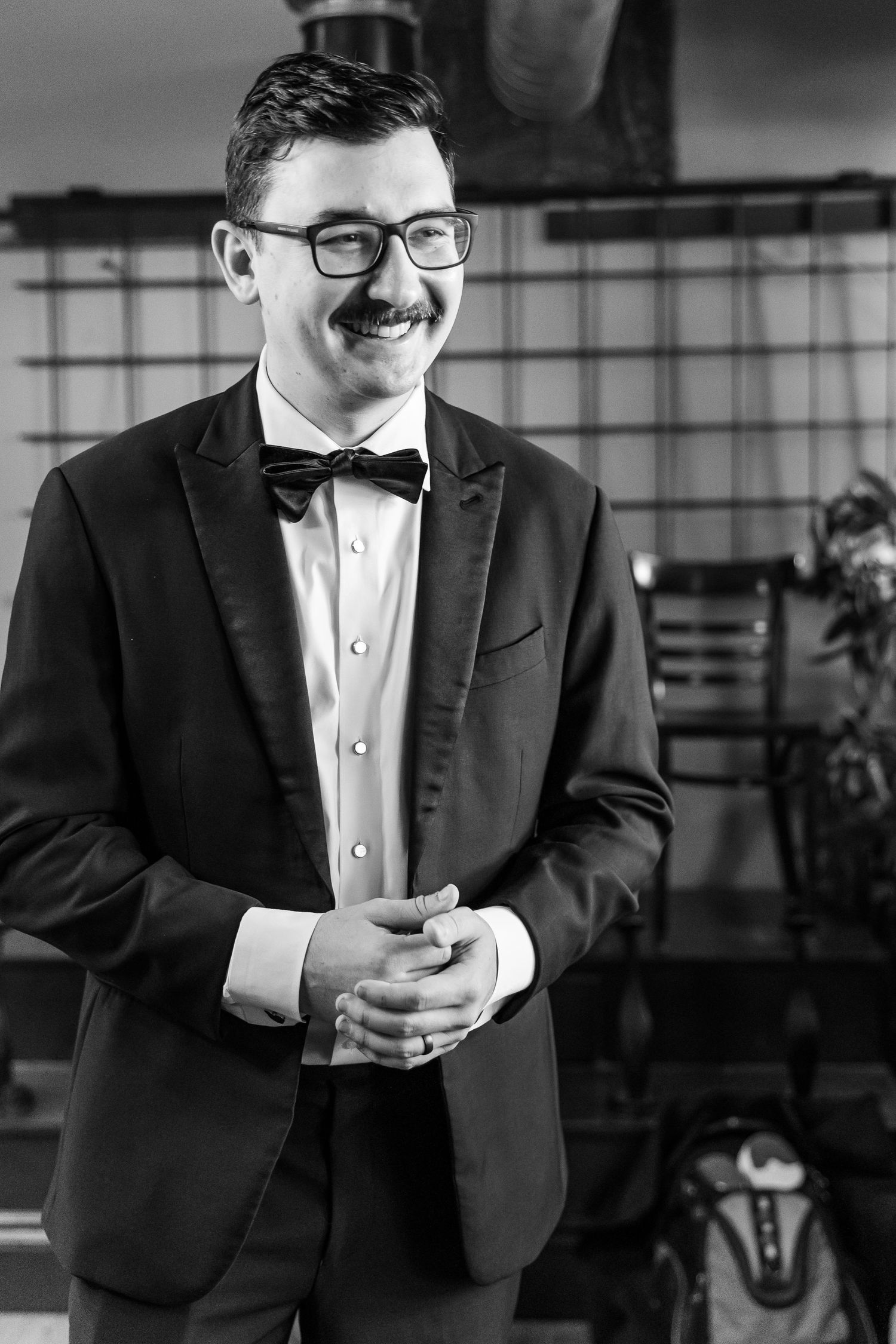 Black and white portrait of a smiling person in formal attire with clasped hands.