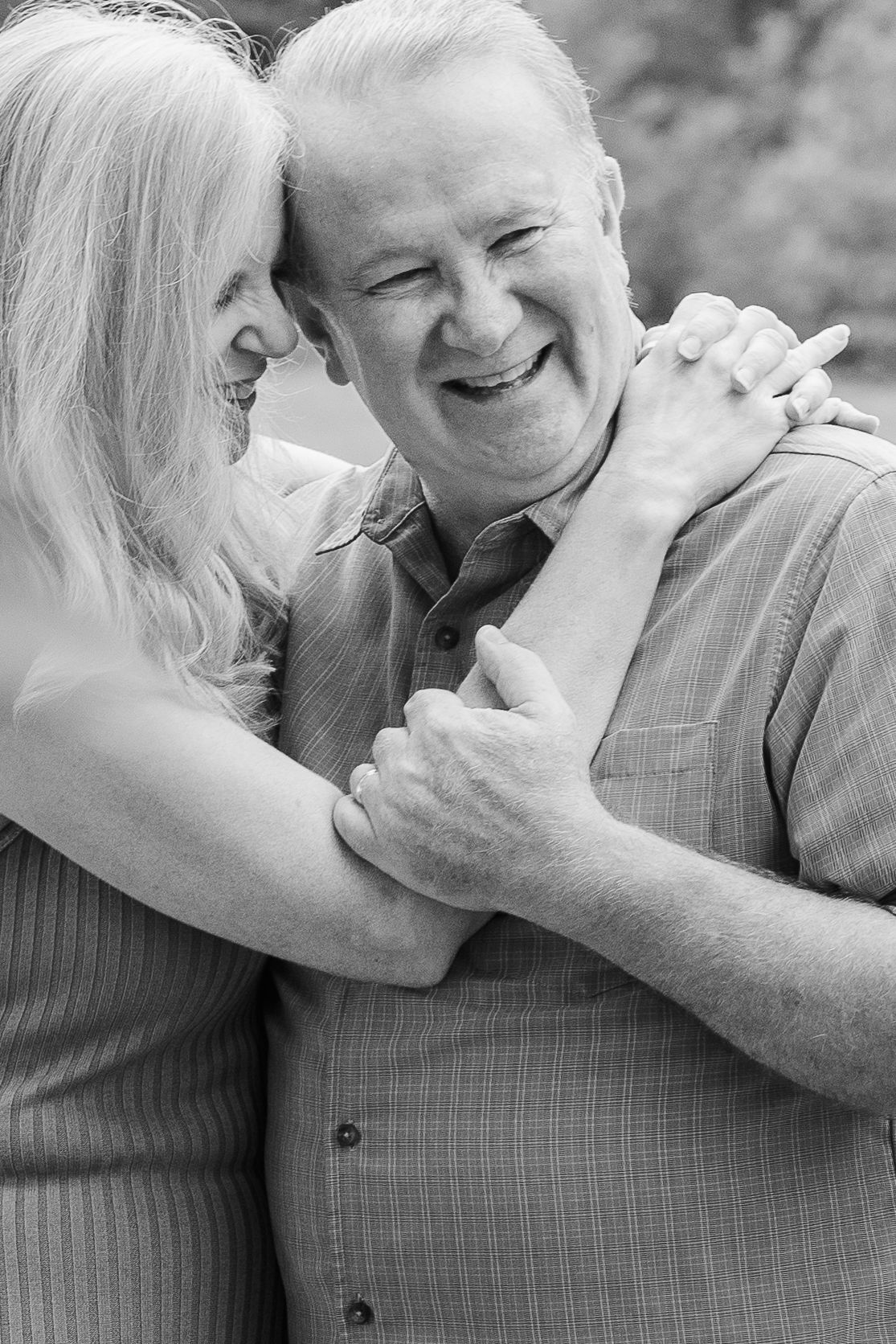 An affectionate senior couple embraces and laughs together in a candid black and white portrait.