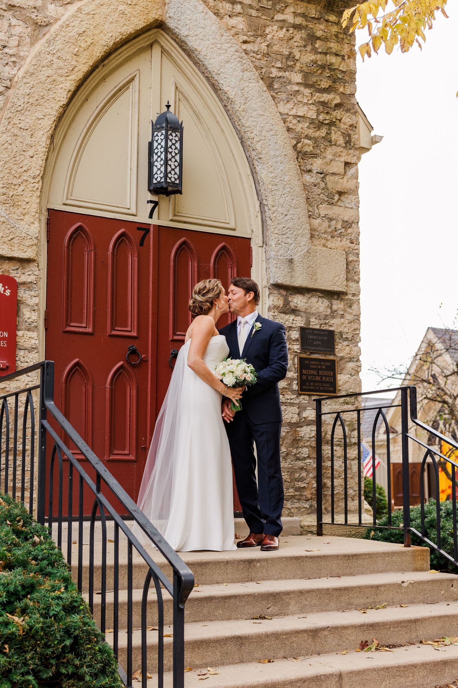 Classic wedding portrait on church steps with stone walls and red door.
